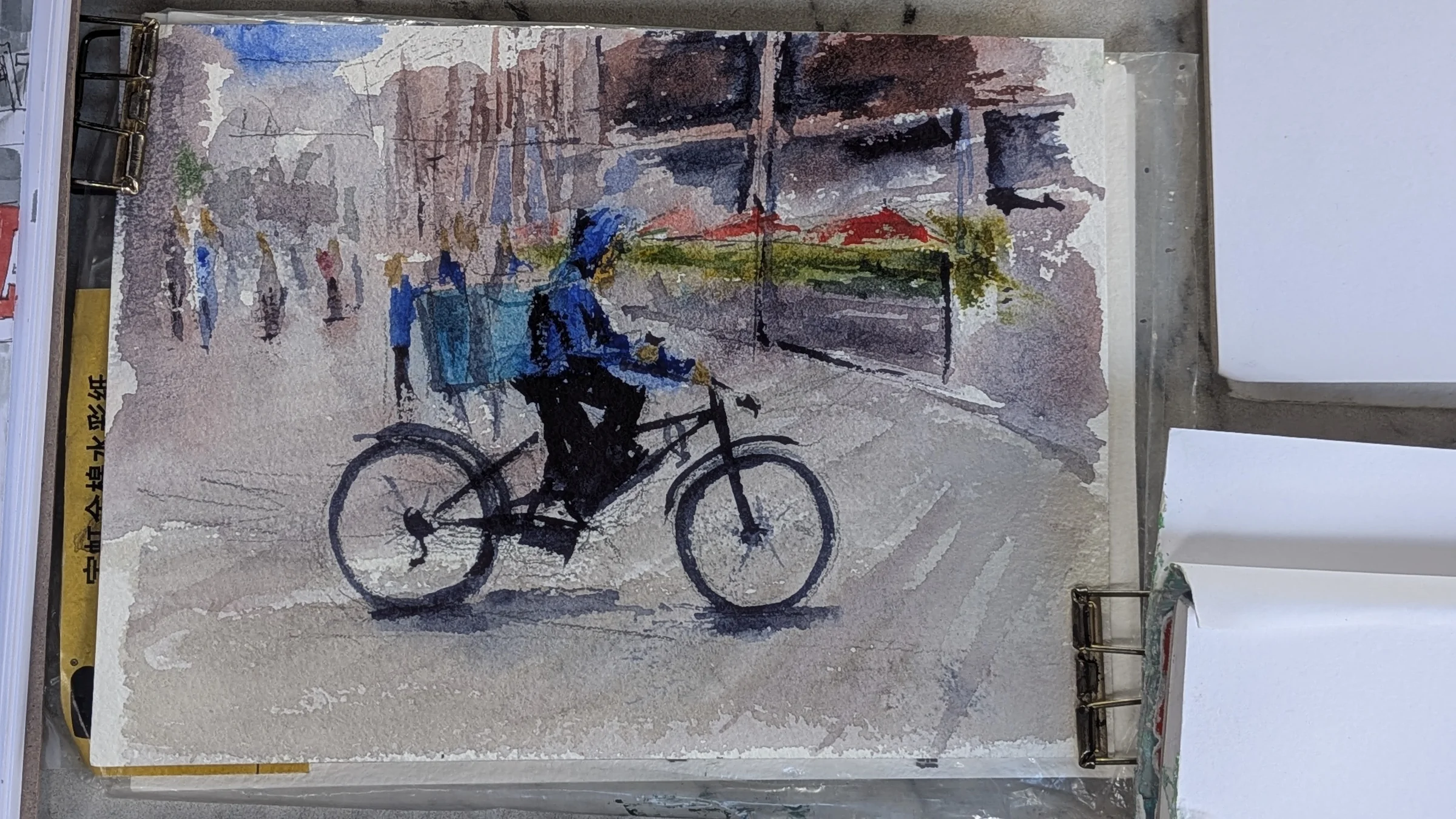 Ink and watercolour: A cyclist with a bright blue cargo box passes through a loosely painted Liverpool street scene.
