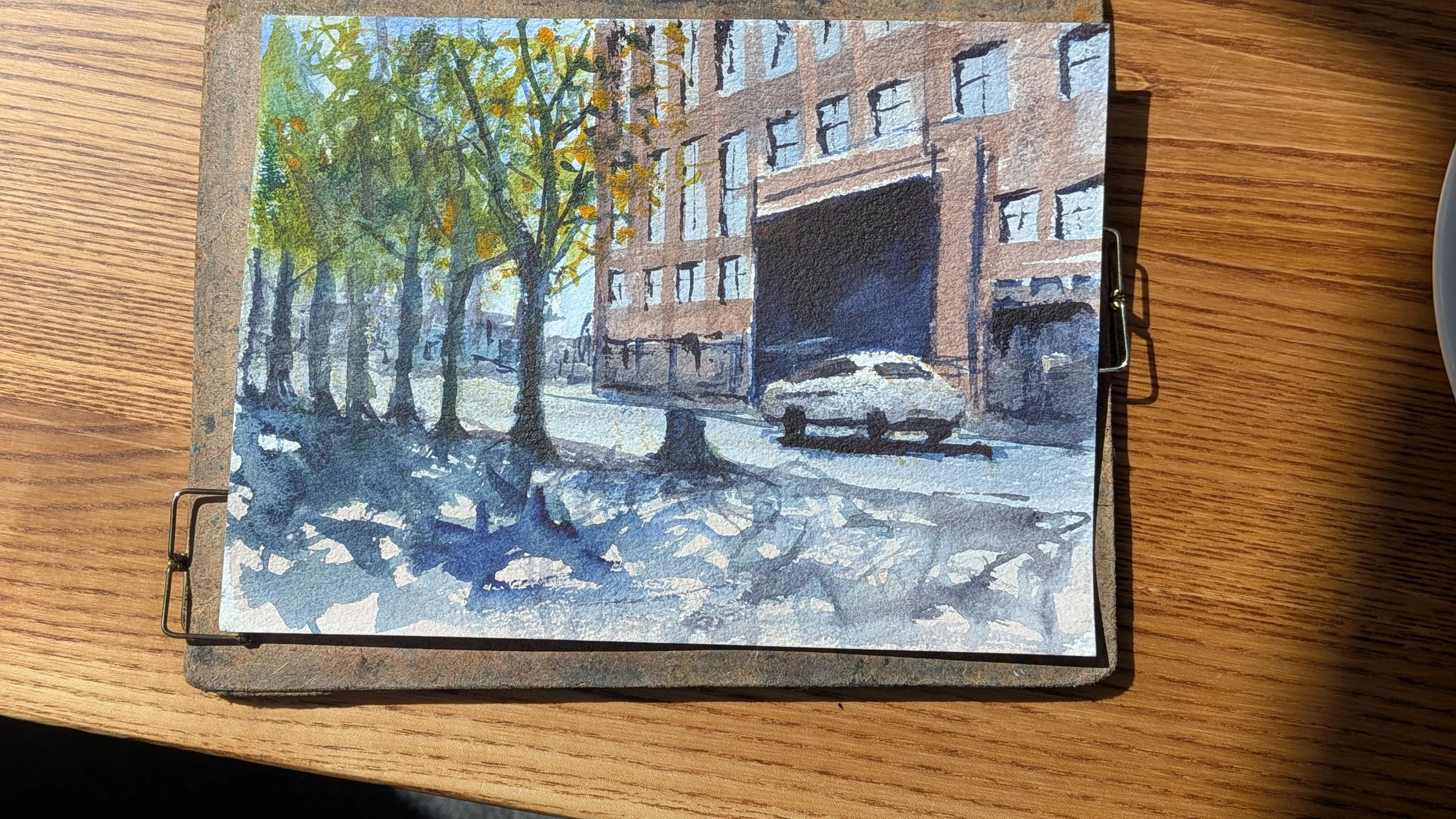 Ink and watercolour: Trees cast dappled shadows across a Liverpool street, with a car beside the red-brick buildings.