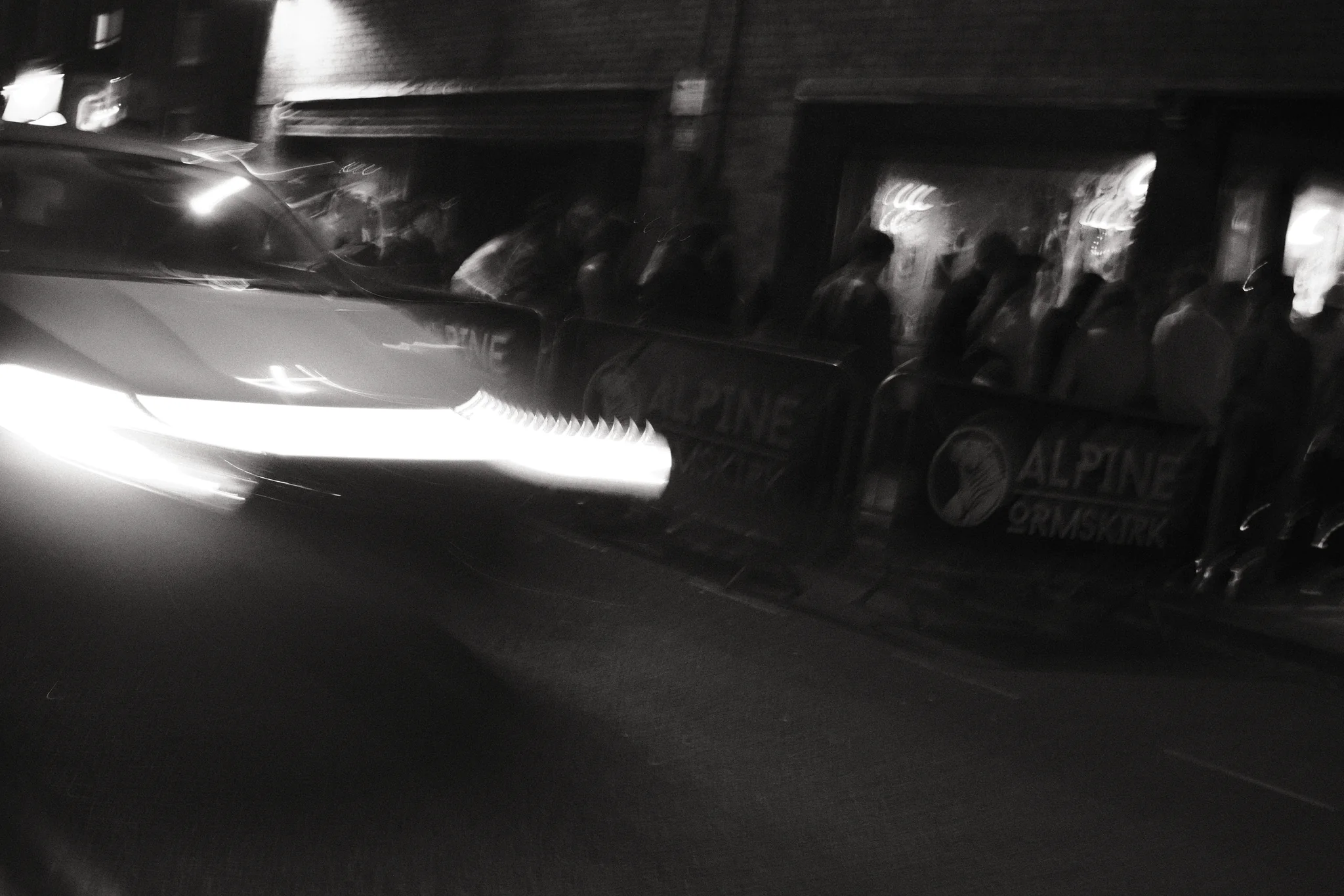 A passing car stretches bright headlight traces across the foreground outside Alpine Ormskirk.