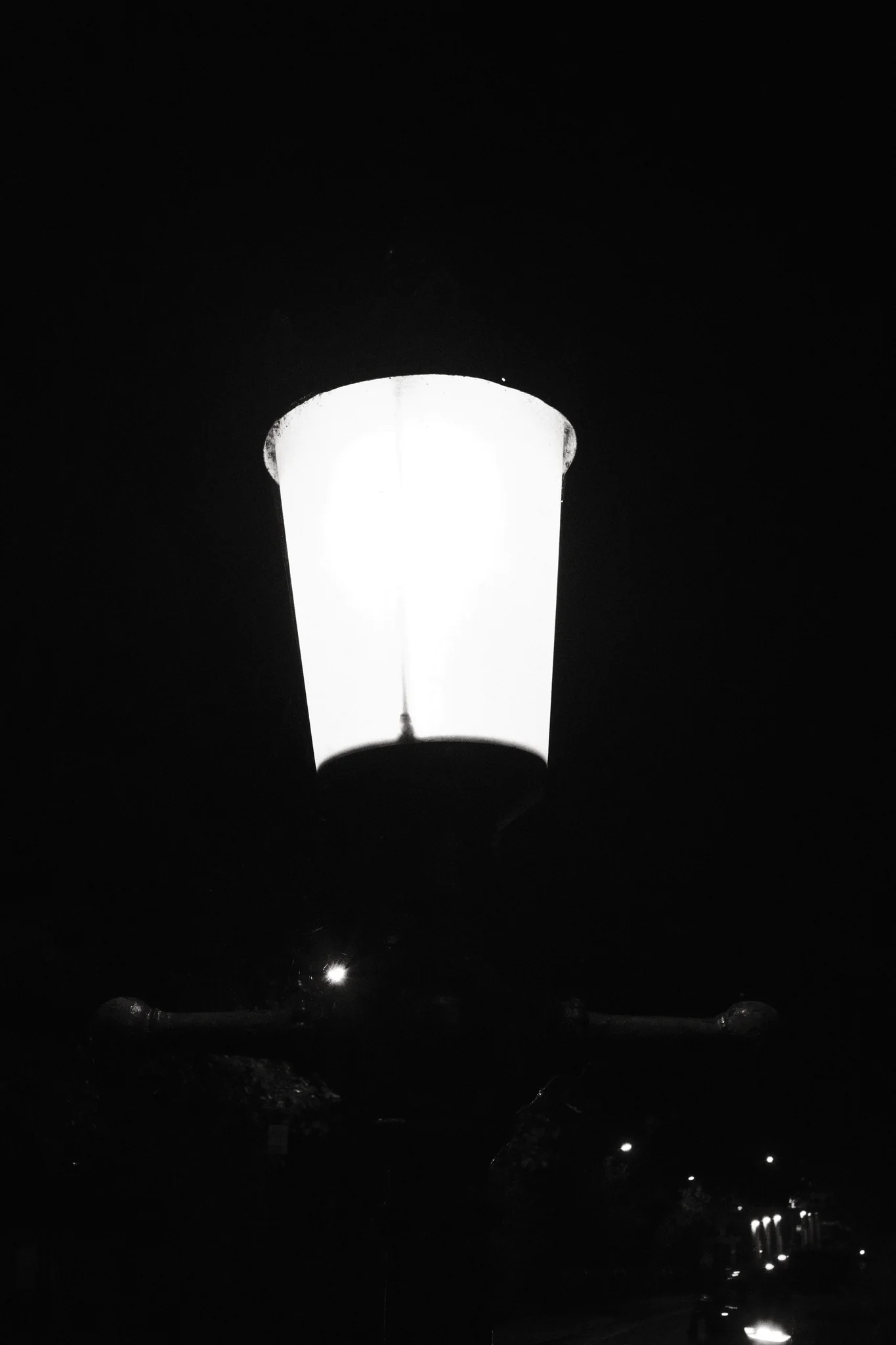 A bright street lamp fills the upper part of a vertical frame, with smaller lights receding into darkness below.
