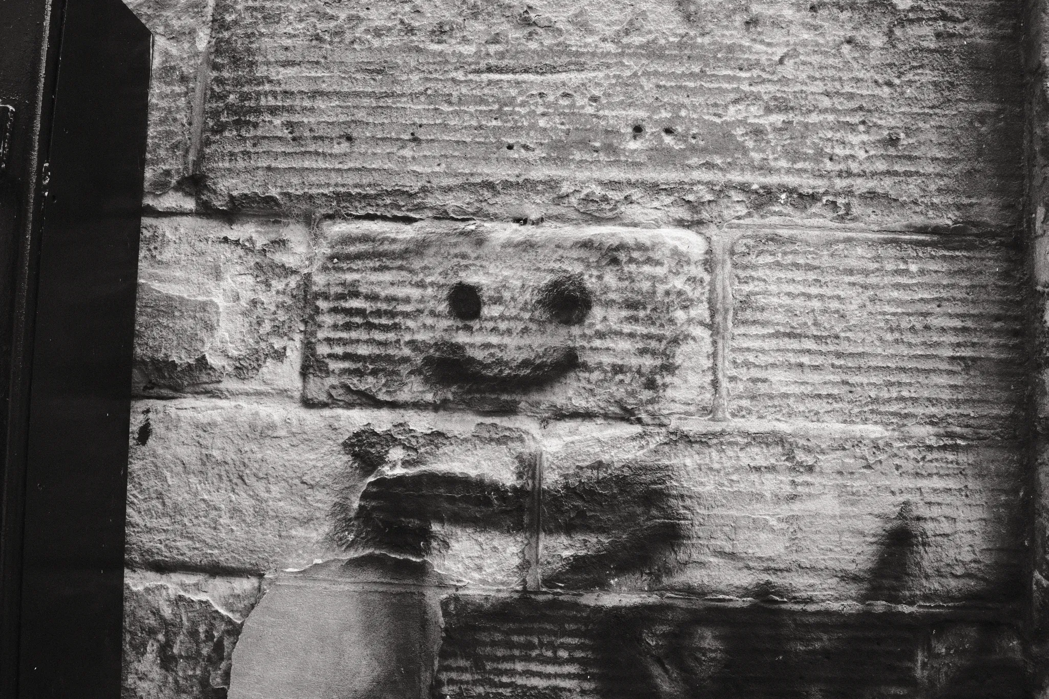 A painted smiling face sits among marks on a textured brick wall.