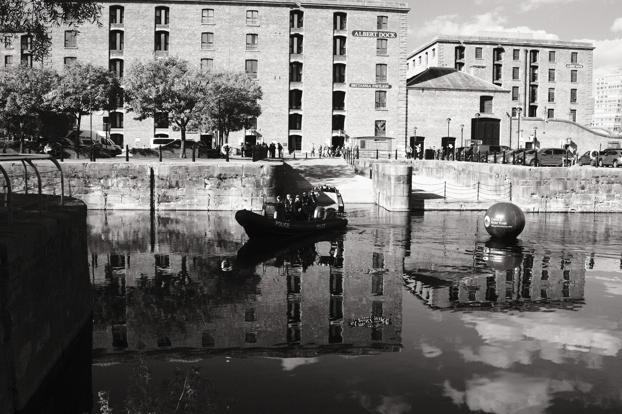 Dock water reflects a moored boat and the buildings beside Royal Albert Dock.