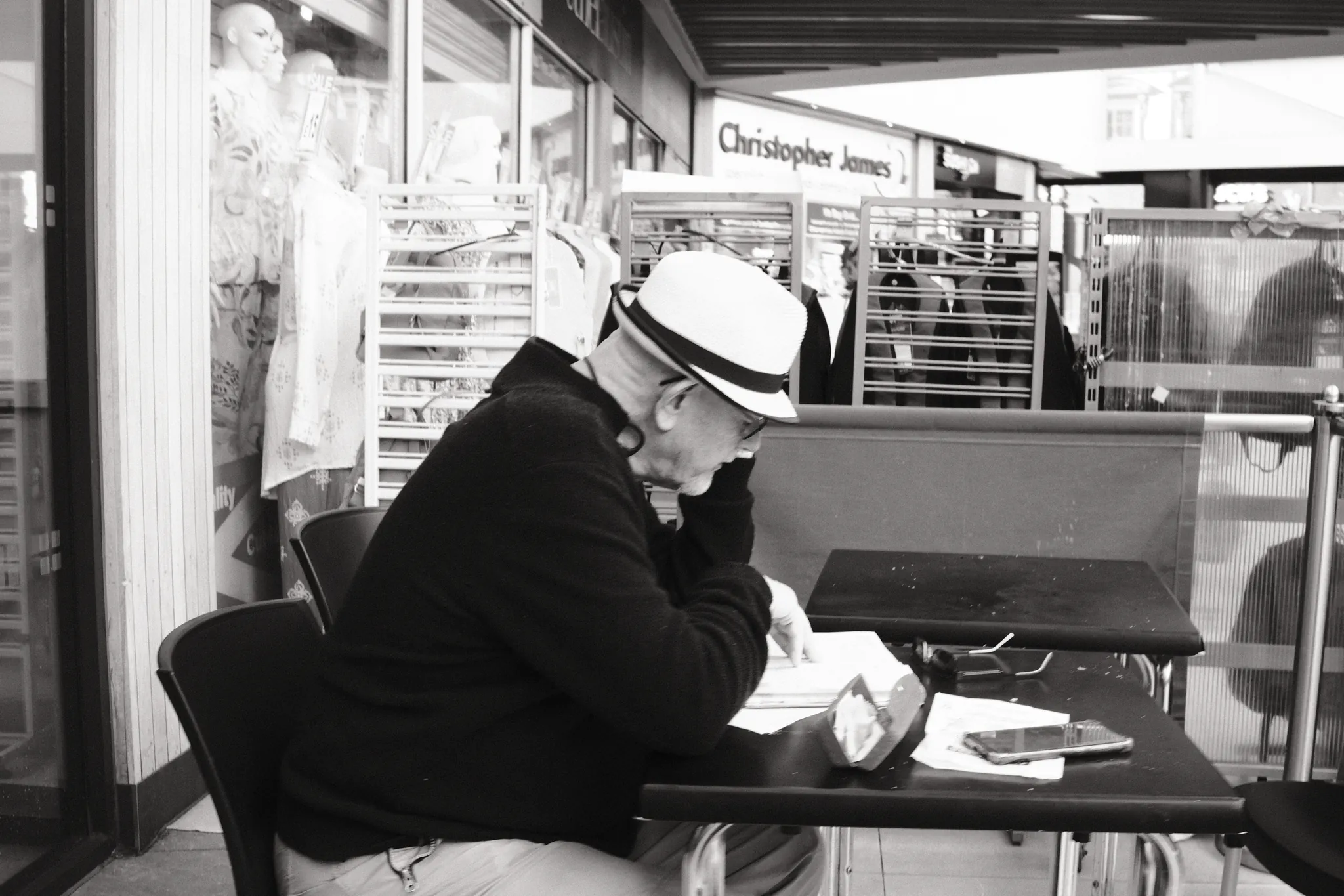 A person in a light hat sits at a café table in a covered shopping space.