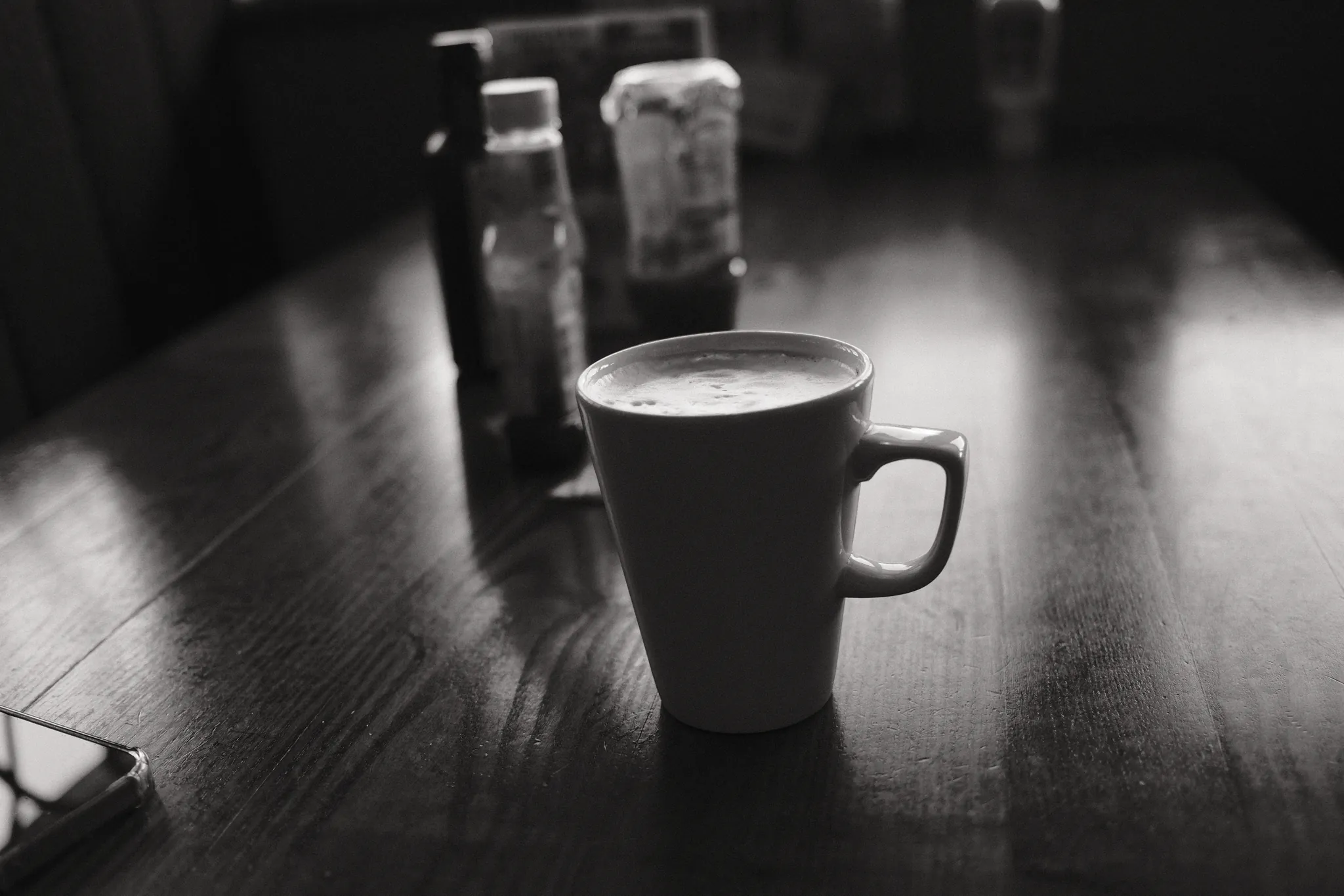 A cup of coffee rests on a dark table beside soft reflected light.