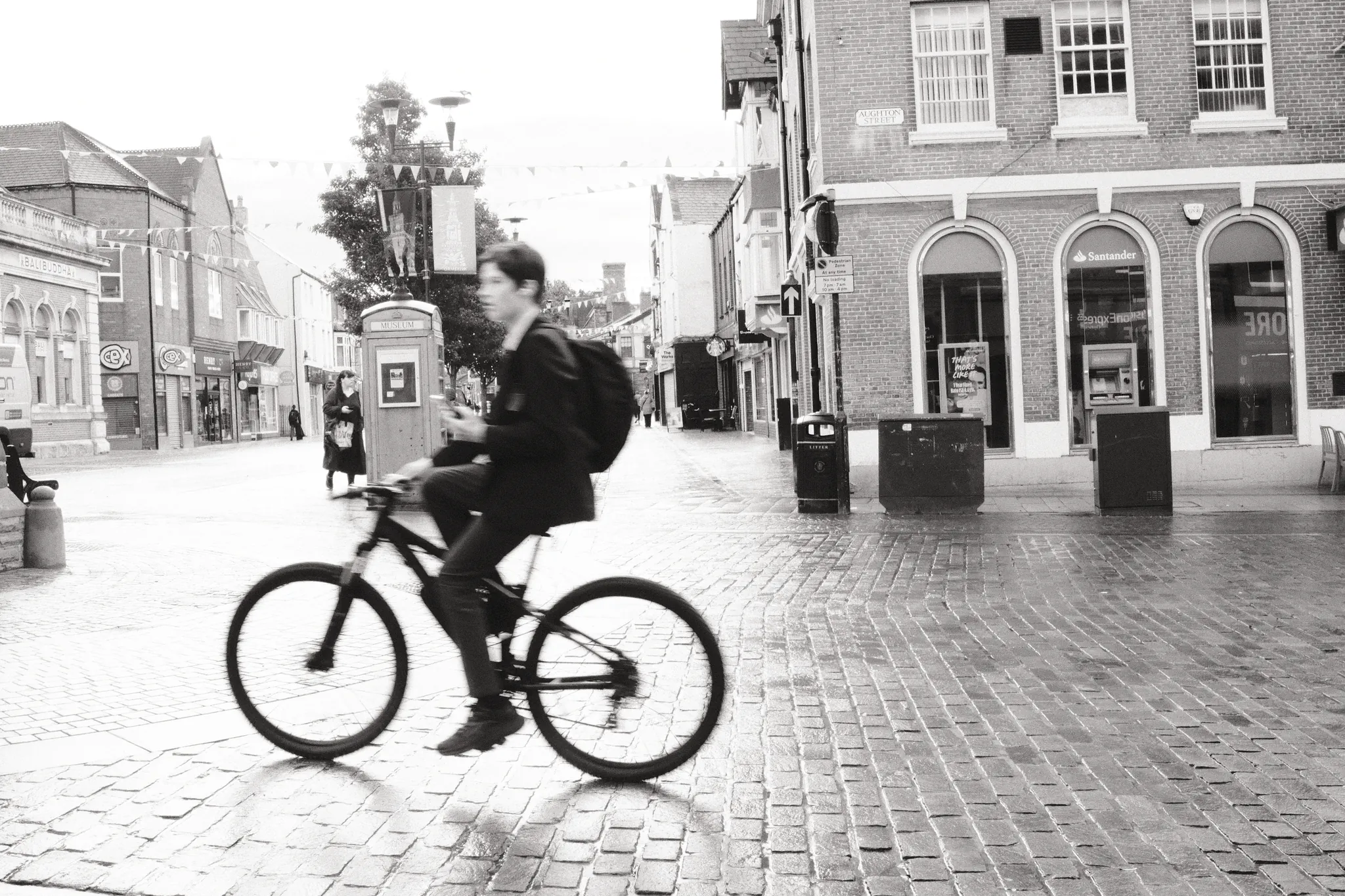 A cyclist crosses the cobbled centre of Ormskirk beside the arched corner shopfronts.