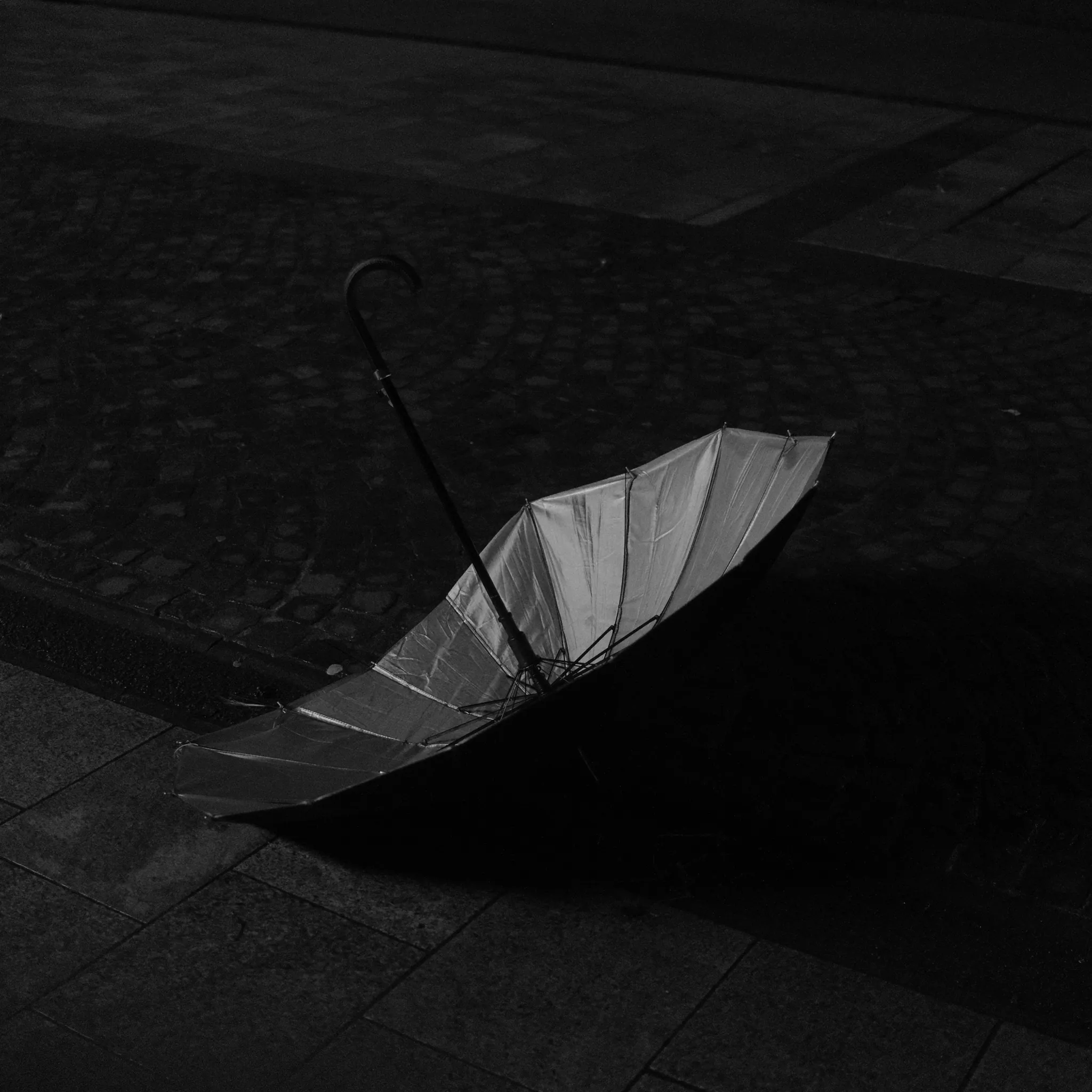 An open umbrella lying on dark paving.