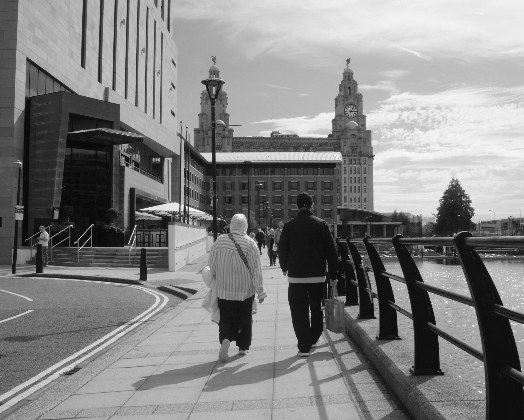 Two people walk along Princes Dock with the Royal Liver Building ahead.