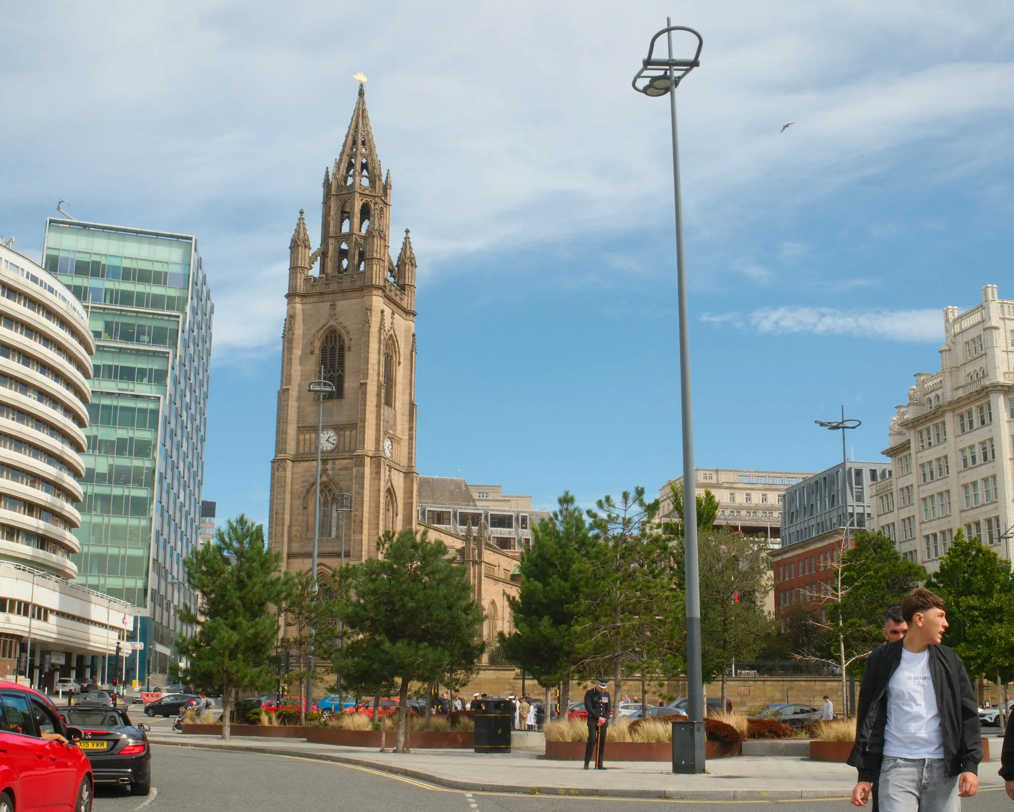 The tower of Our Lady and St Nicholas rises above trees, traffic and pedestrians near Liverpool’s waterfront.