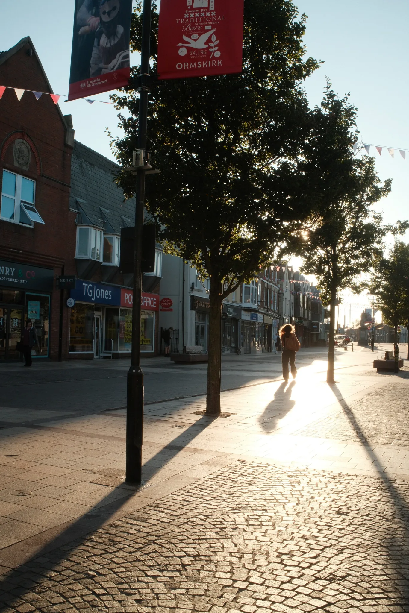 Warm evening light falls along Moor Street in Ormskirk, past the shops and Post Office.