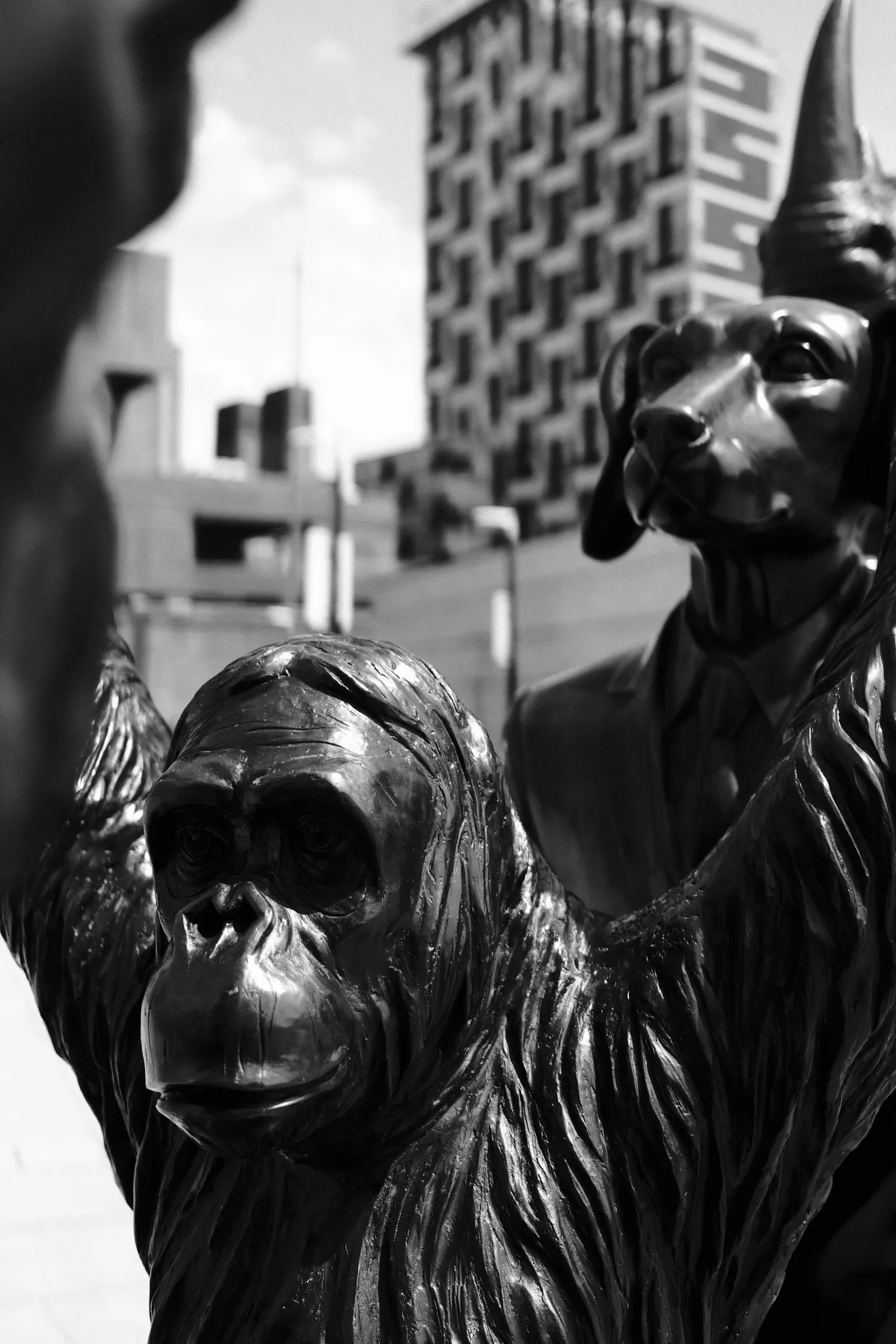 A chimpanzee sculpture fills the foreground, with another sculpted figure and modern buildings behind it at Princes Dock.