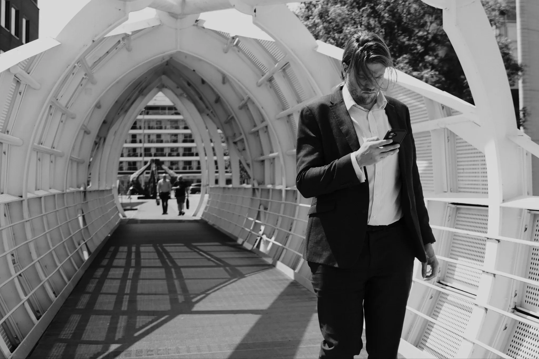 A person checks a phone beneath the repeating white arches of Princes Dock footbridge.