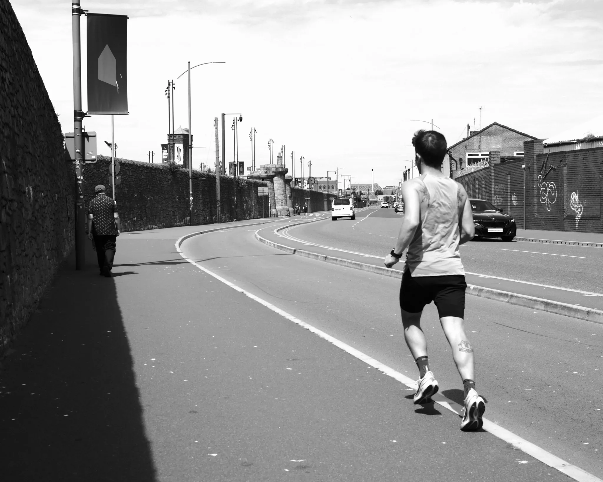A runner following the bend of a road, photographed in black and white.