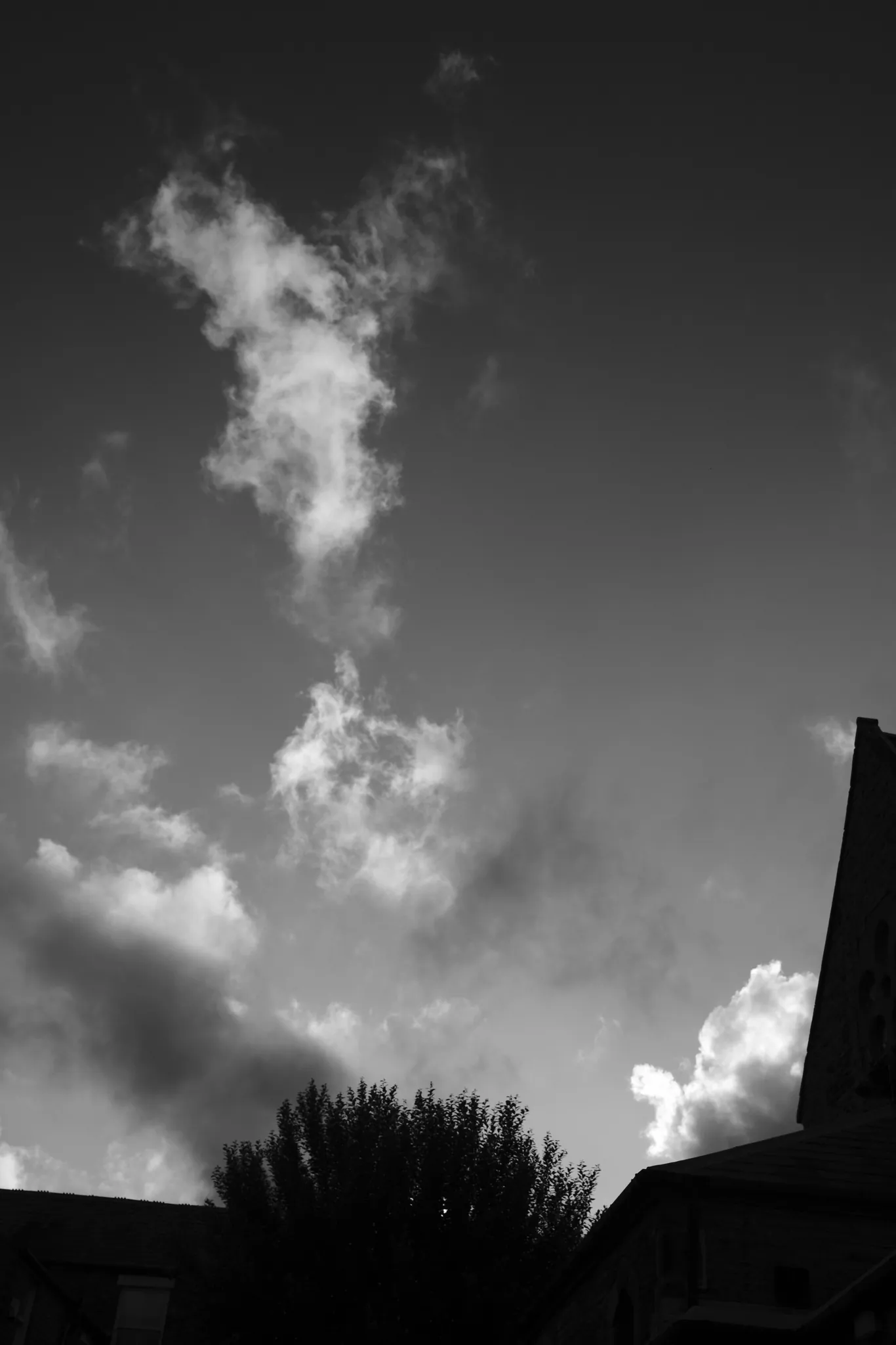 A bright cloud against a dark sky above roof silhouettes, in black and white.