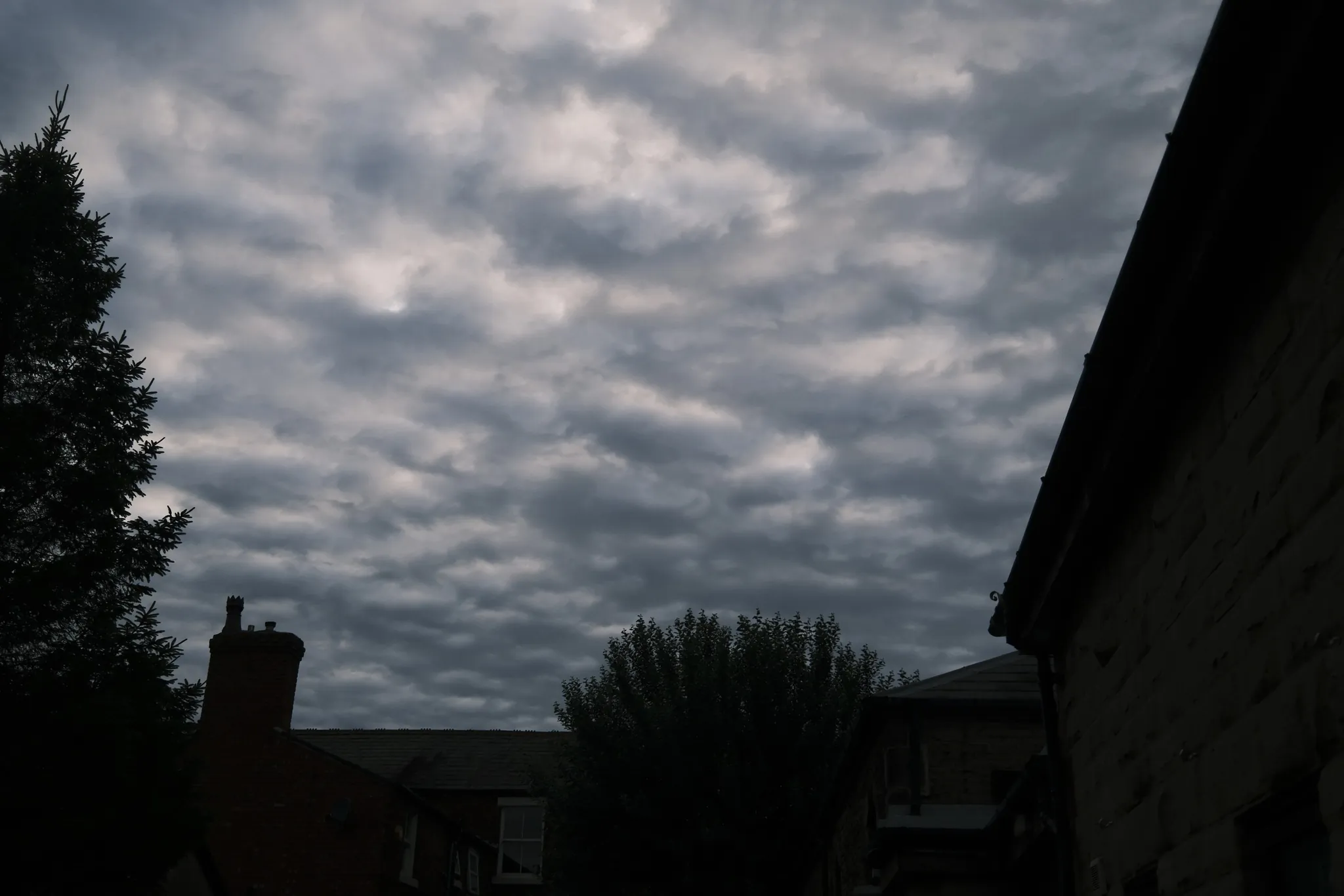 Layered clouds over a garden and dark rooftops.