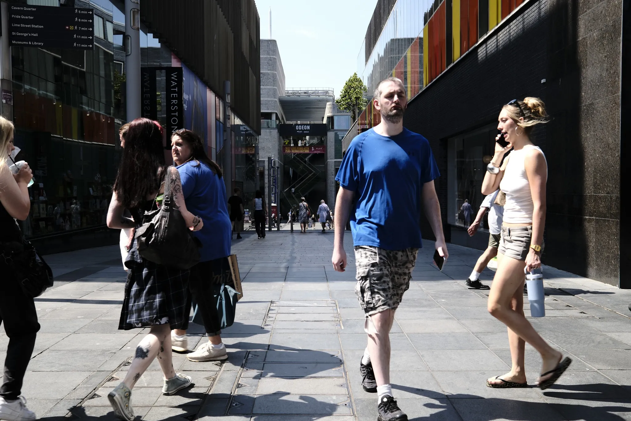 Pedestrians cross a sunlit shopping street between Waterstones and the Odeon at Liverpool ONE.