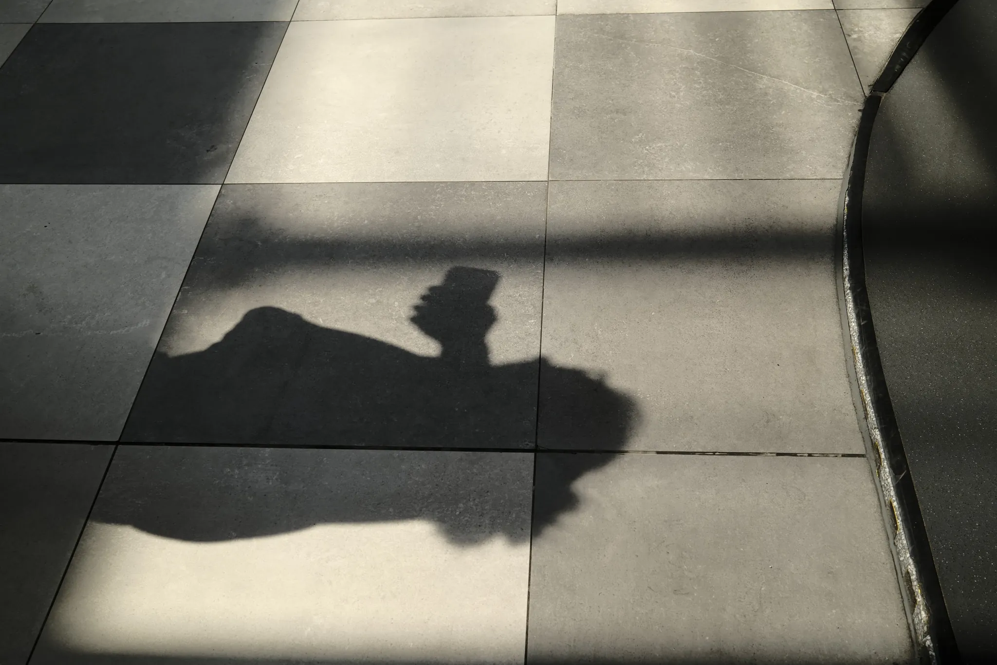 A human shadow crossing a grid of sunlit floor tiles.