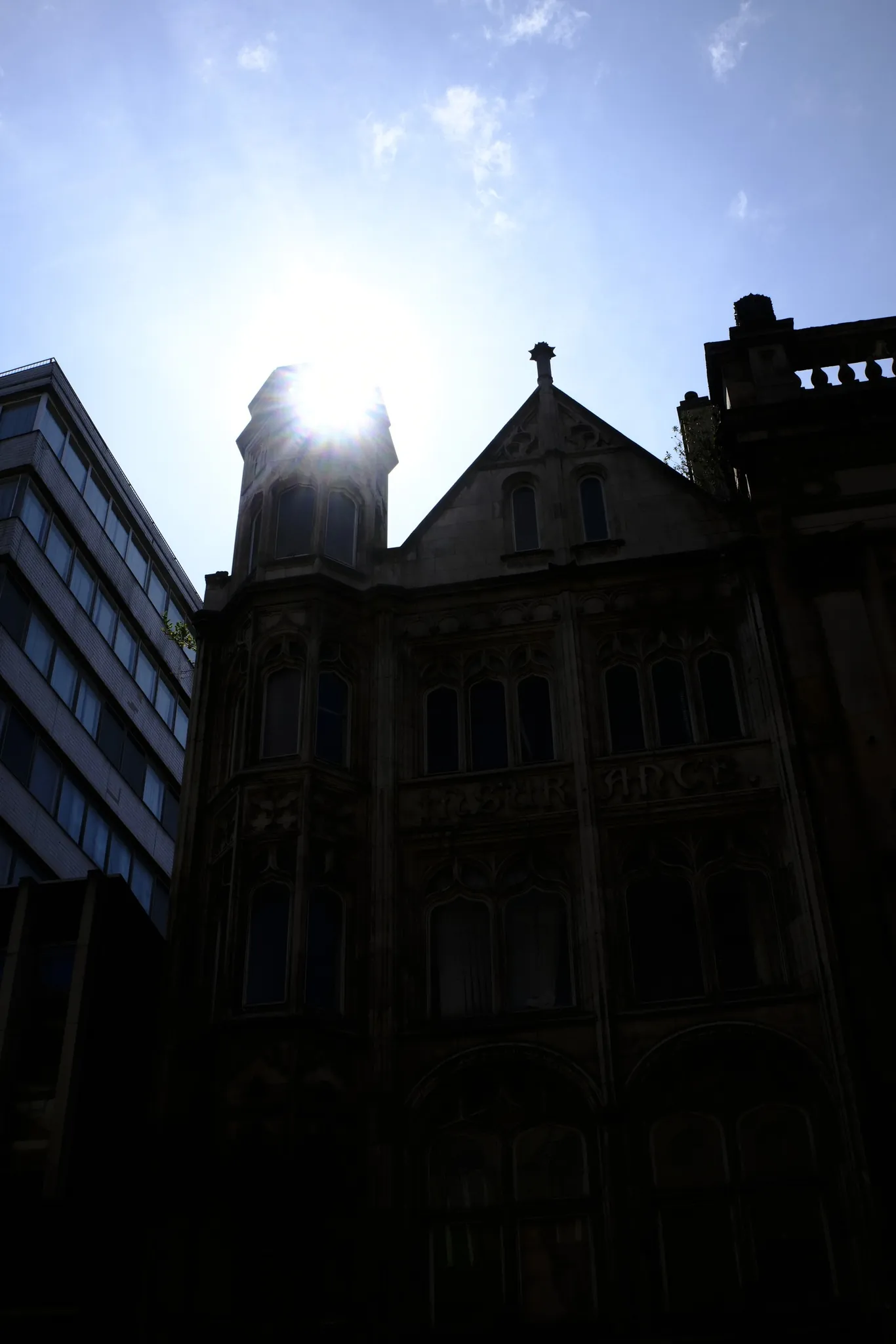 The sun breaking around a dark historic roofline.