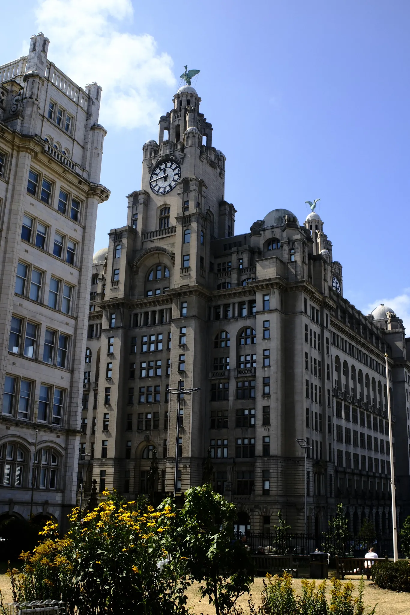 Flowers in front of the Royal Liver Building beneath a blue sky.