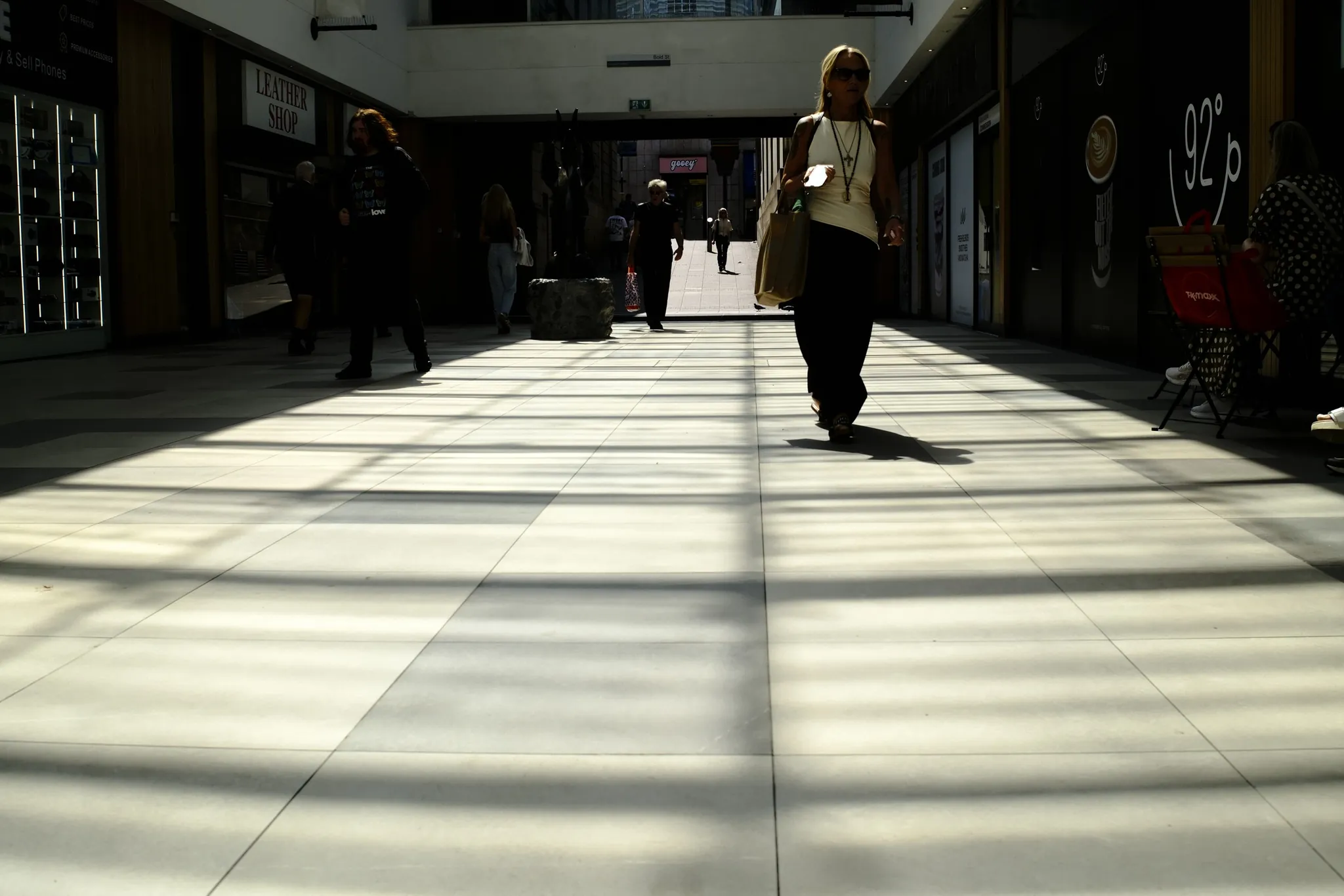 Pedestrians crossing a grid of sunlight inside a shopping arcade.