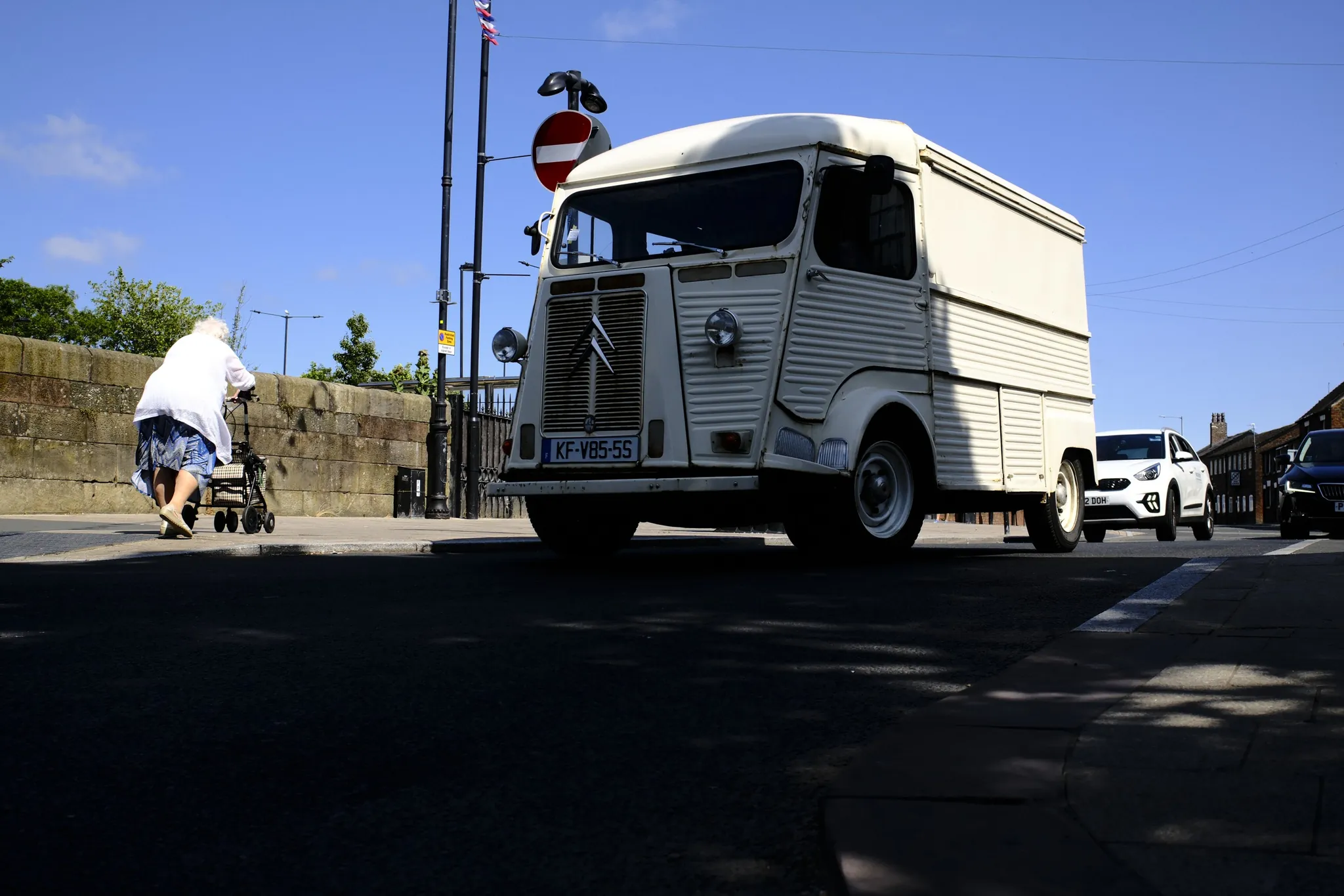 A pale vintage van passing a crossing under a clear blue sky.