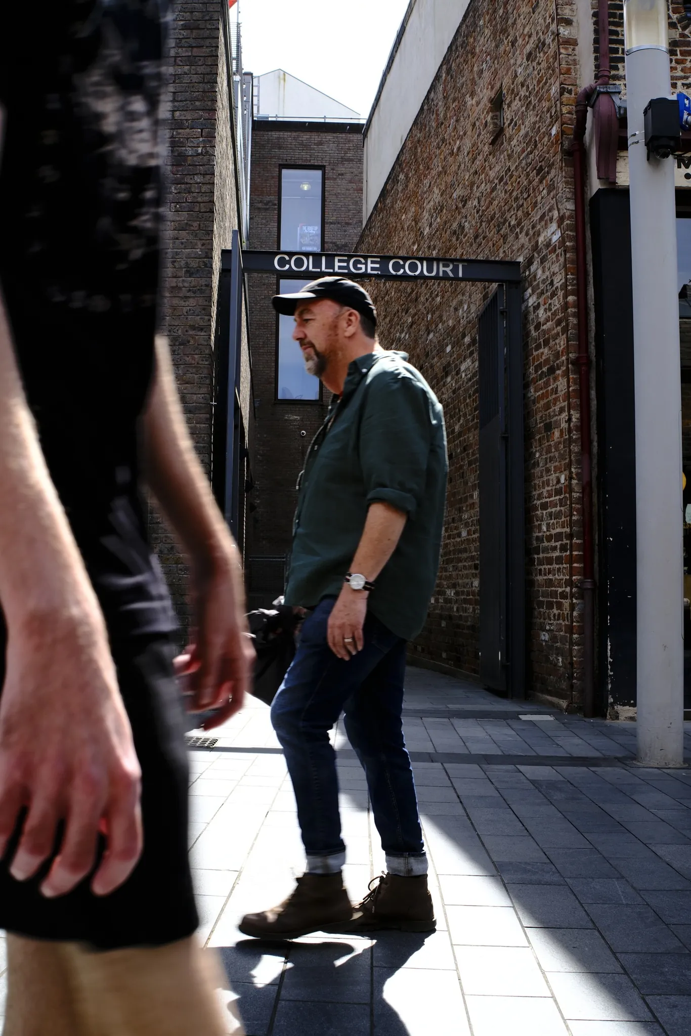 A pedestrian crosses a patch of sunlight beside the College Lane street sign at Liverpool ONE.