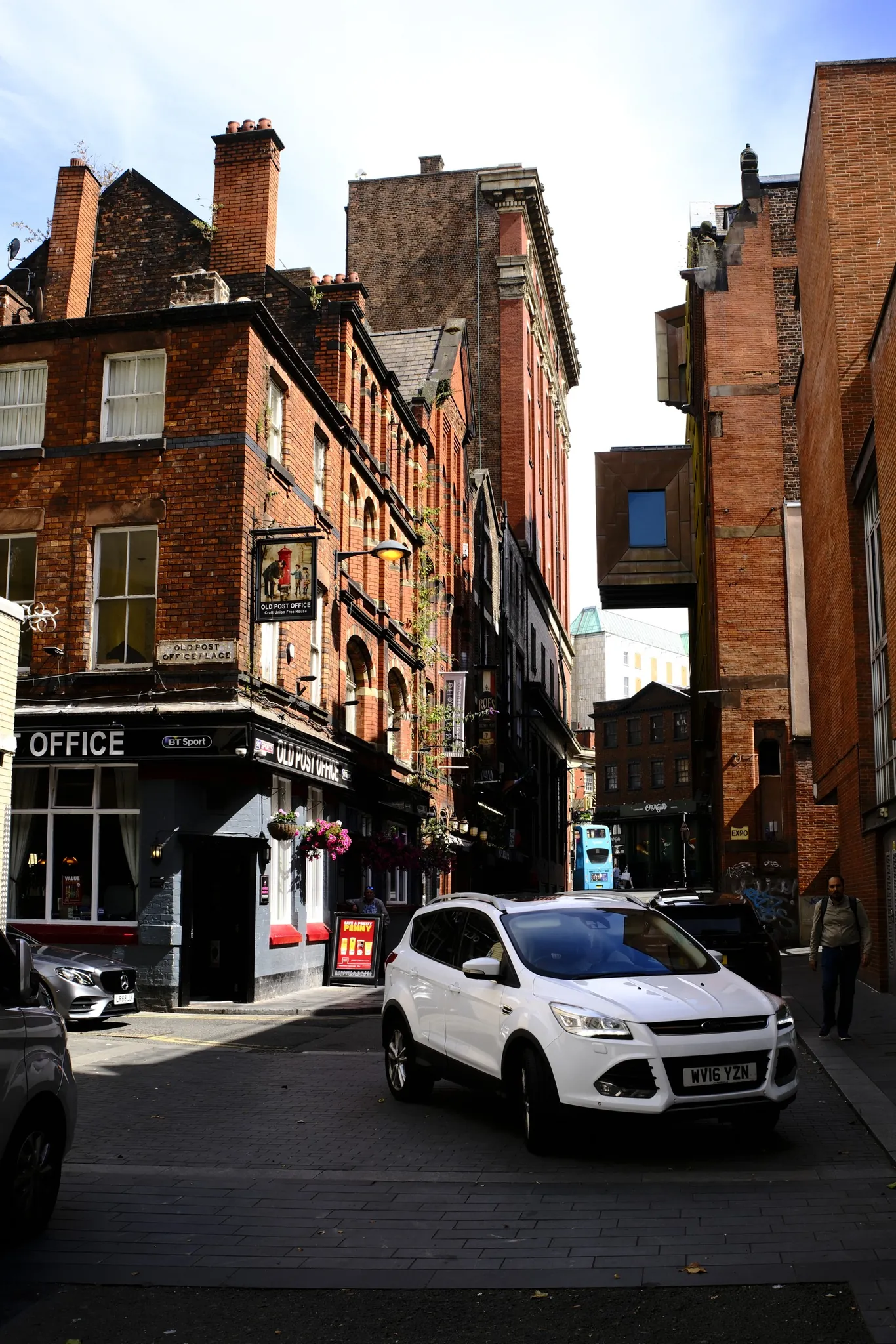 A white car turns beside the Old Post Office pub on a narrow Liverpool street.