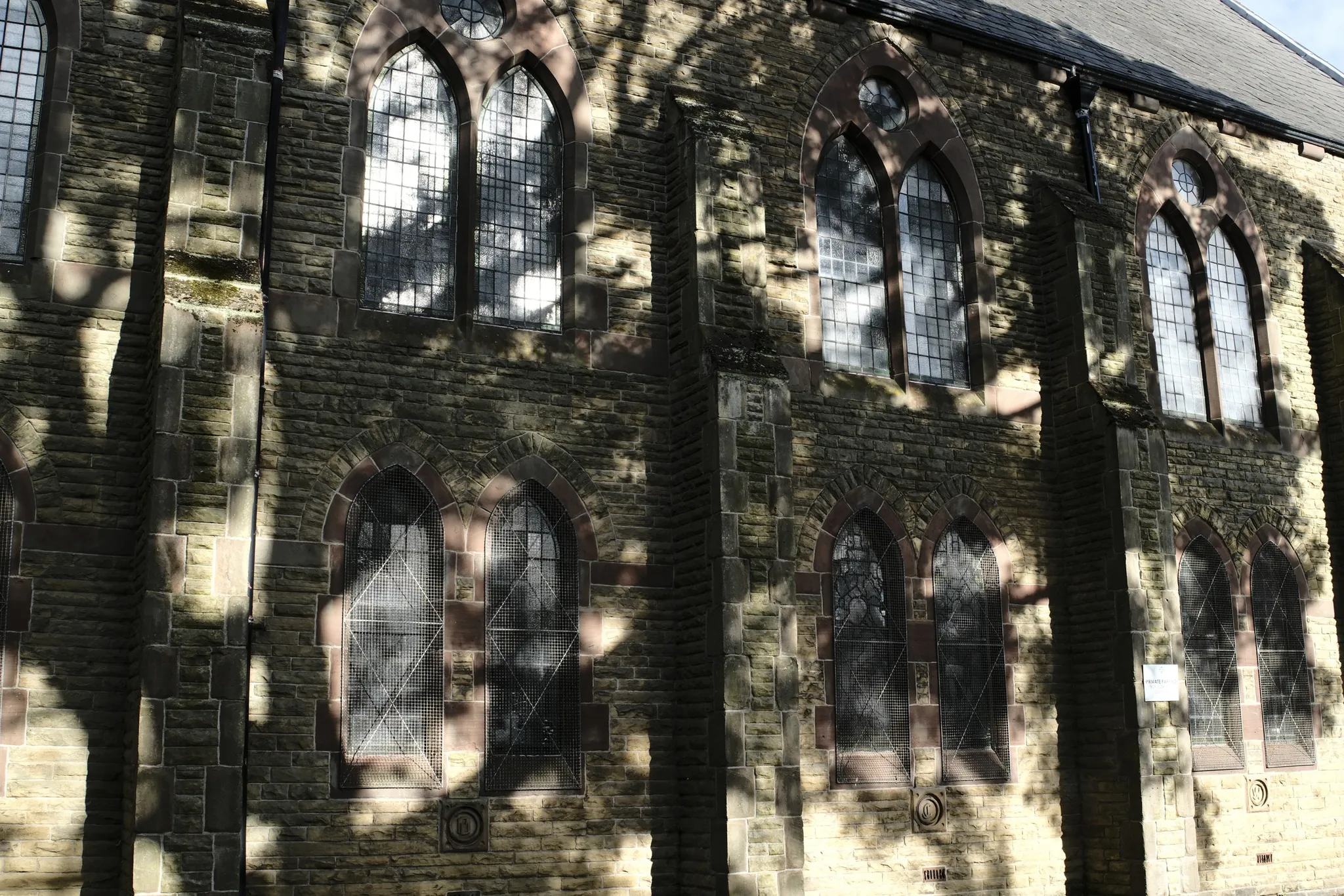 Leaf shadows falling across a stone facade with arched windows.