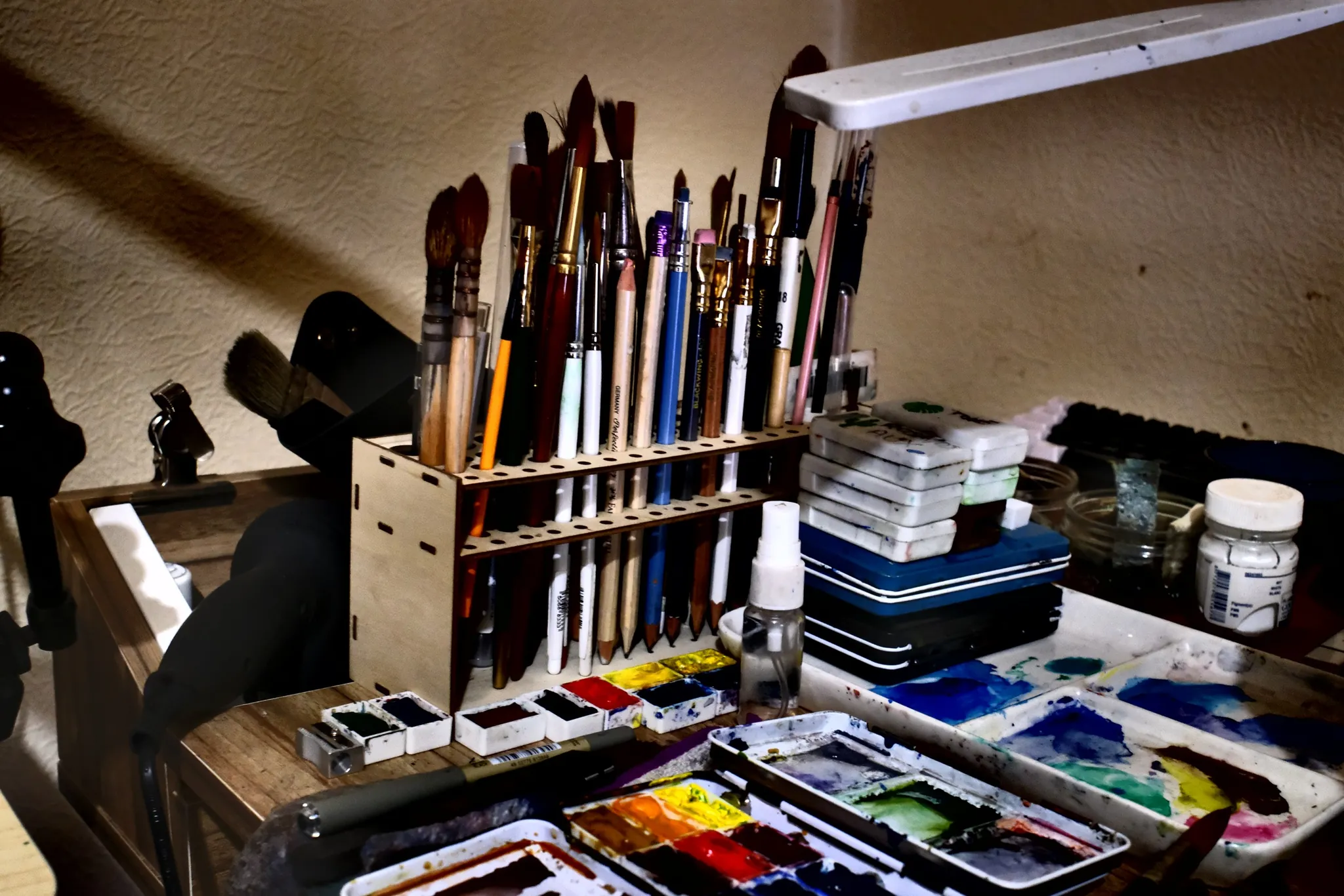 Brush racks, paint palettes and tins arranged on a studio work surface.