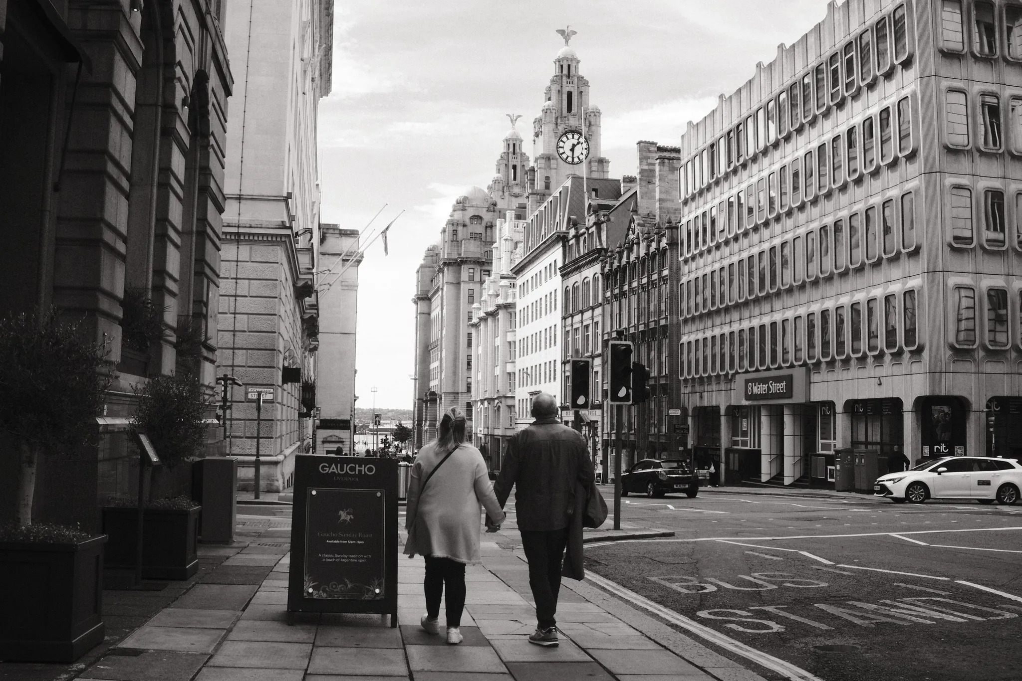 Two pedestrians walk down Water Street towards the Royal Liver Building.