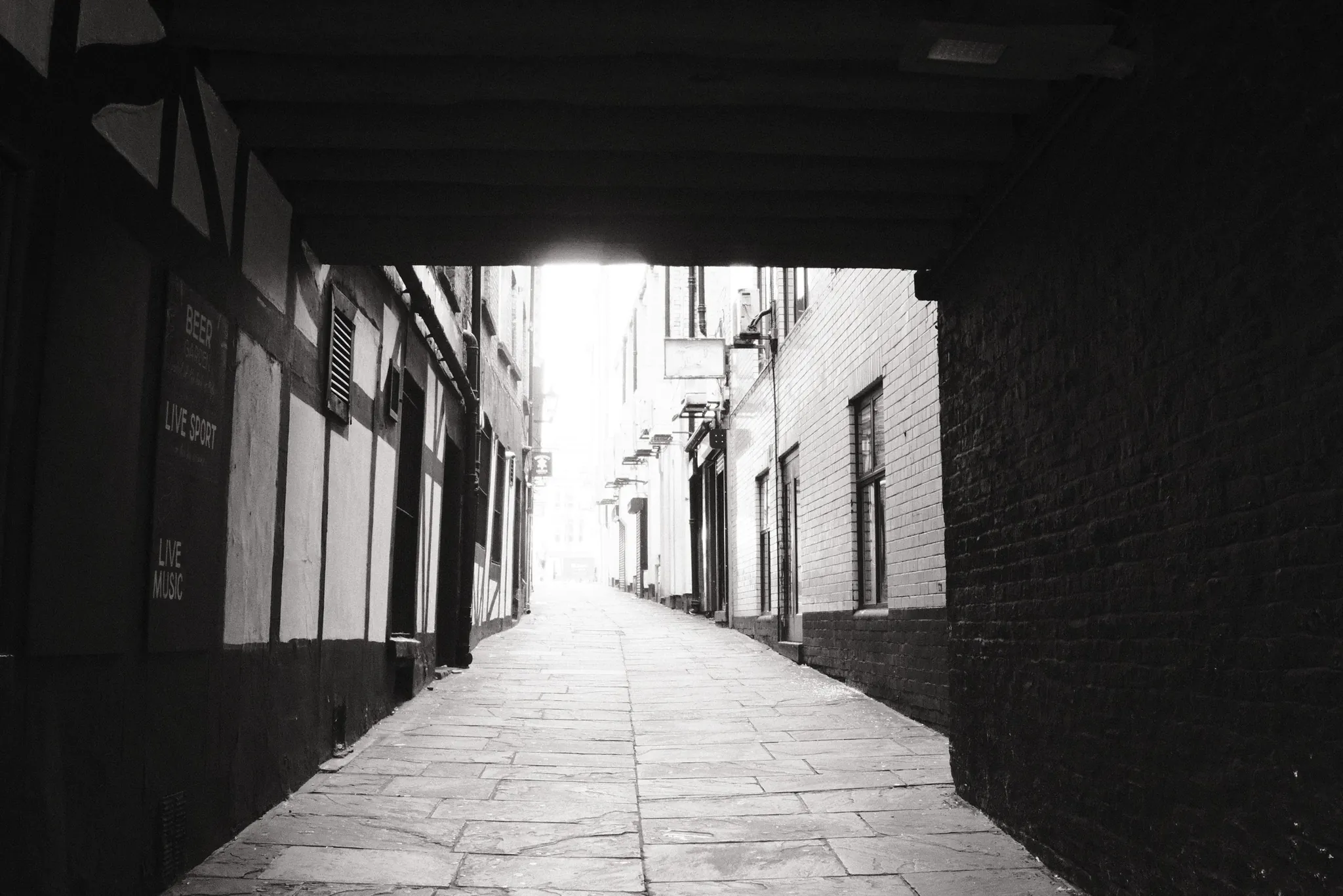 A narrow paved lane emerging from the shadow of an overhead structure.