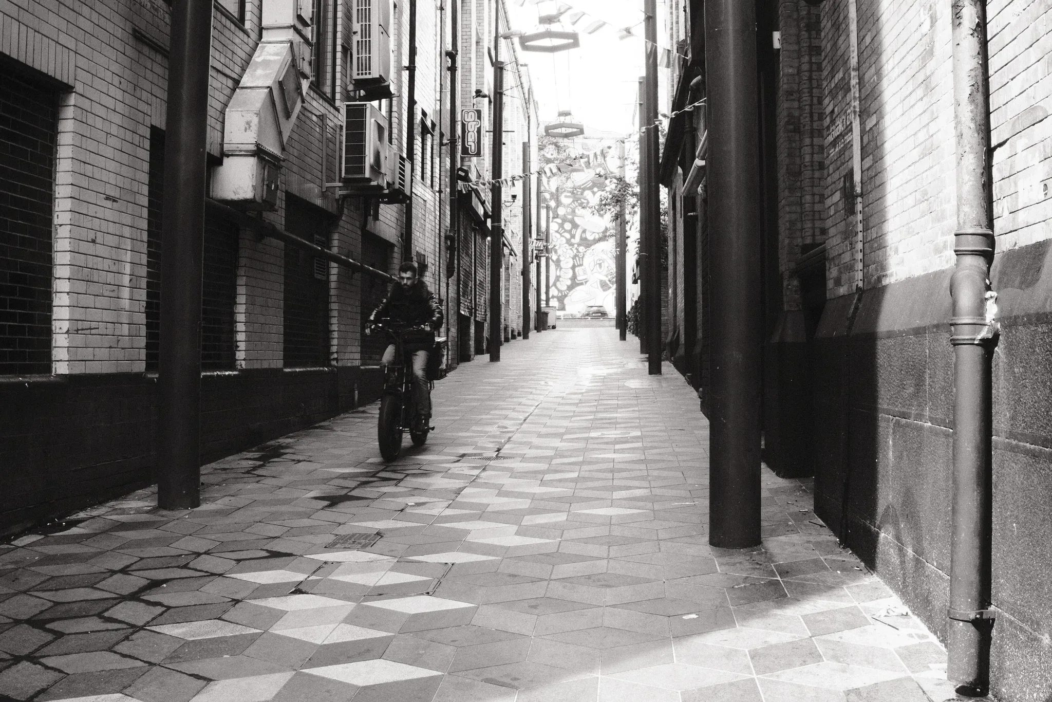 A pedestrian in a narrow lane paved with patterned tiles.