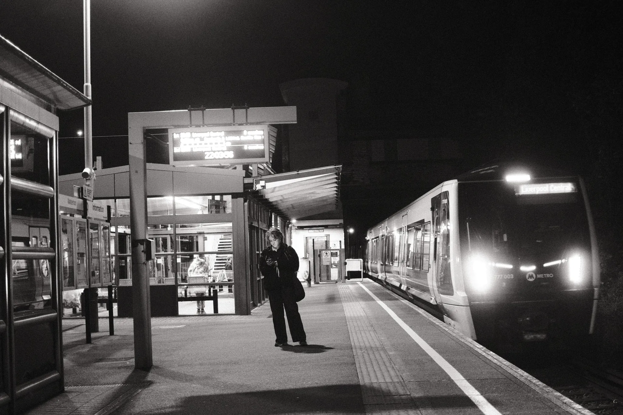 A train with bright headlights approaching a person on the platform.