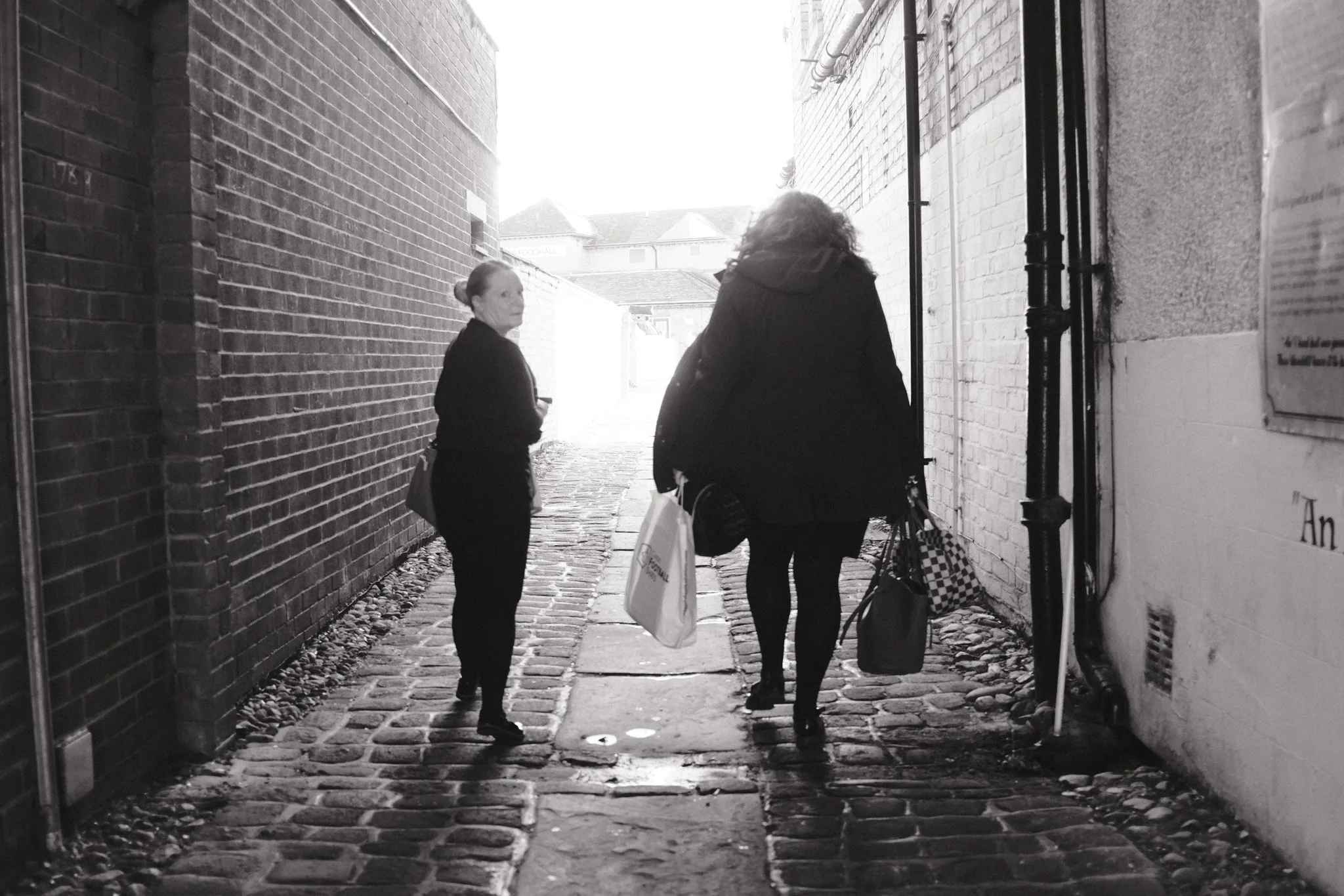 People walking along a cobbled passage towards a bright opening.