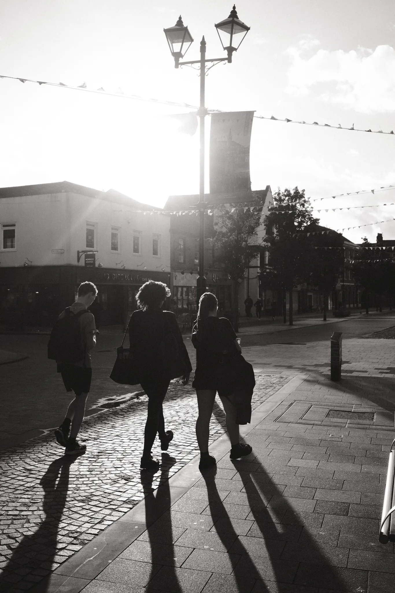 Three pedestrians cast long shadows across the paving in Ormskirk town centre.
