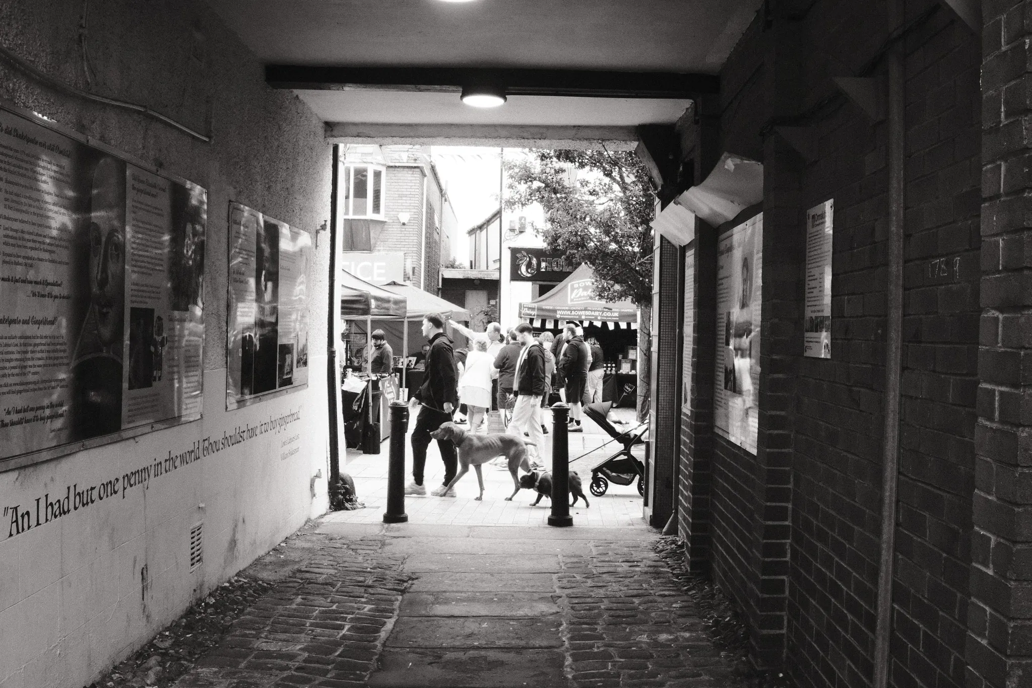 A shaded passage opening onto people and shops in daylight.