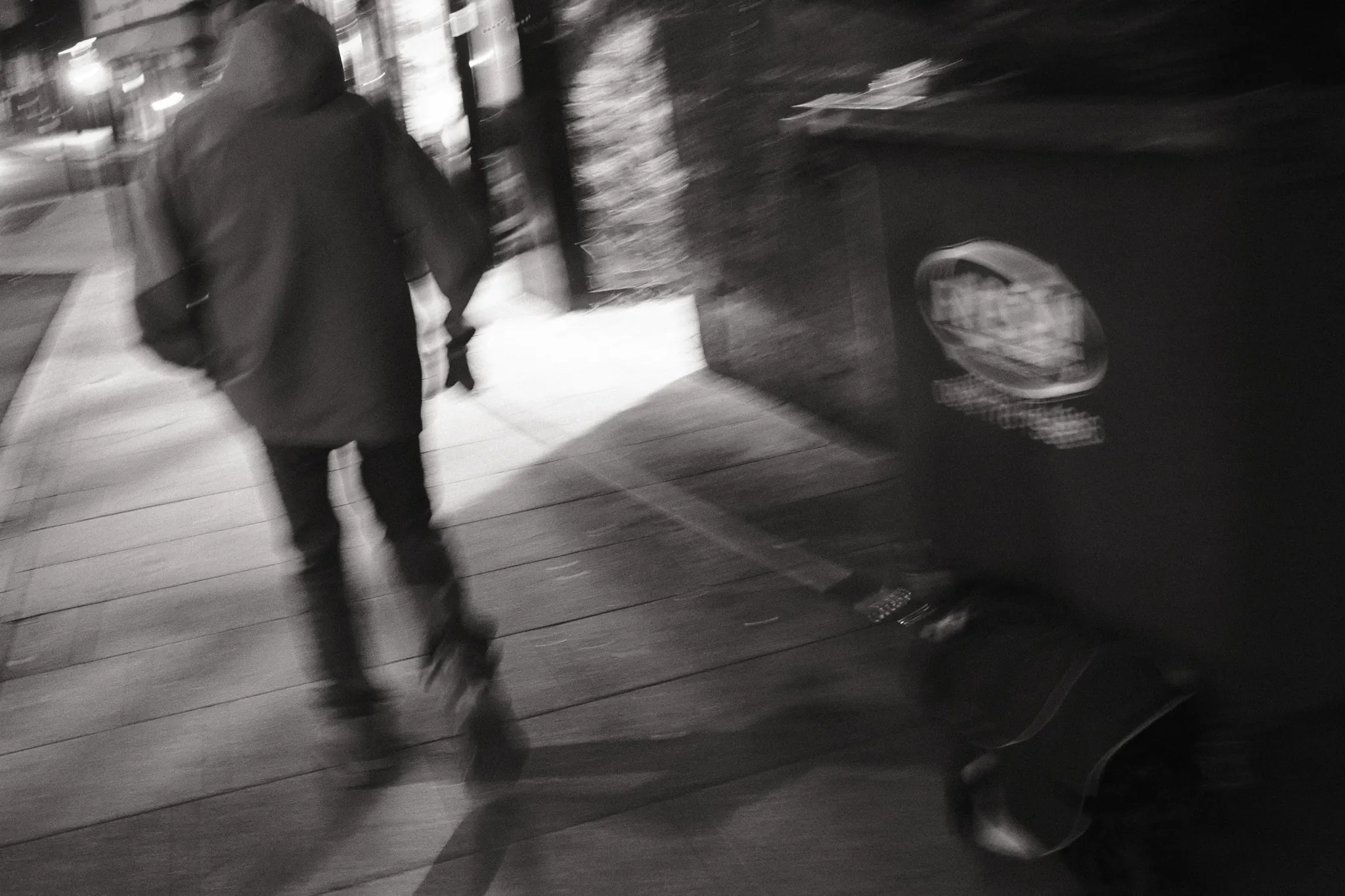 A blurred pedestrian moving past street furniture.