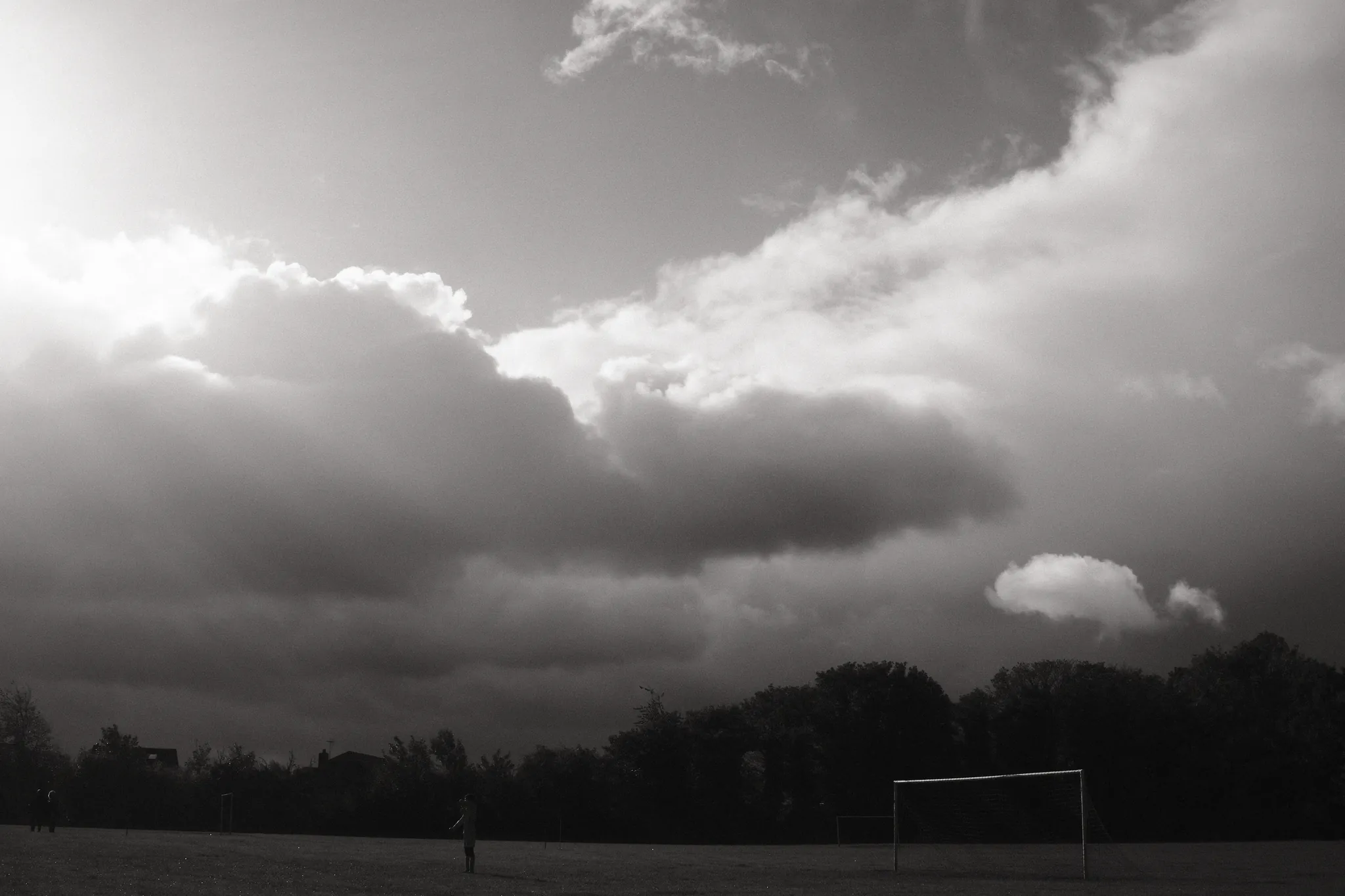 Light breaks through heavy clouds above an open playing field.