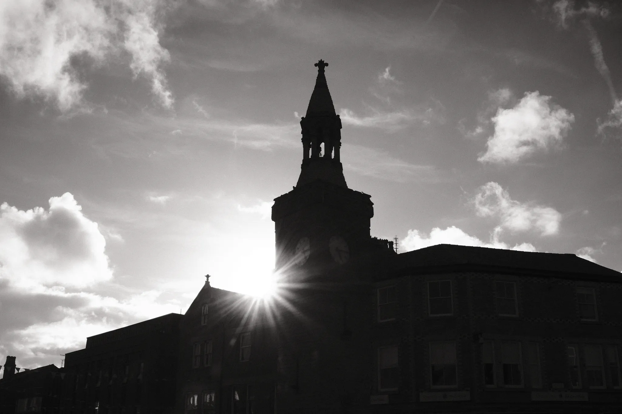 Sunlight breaks around a roofline beside the silhouette of Ormskirk Clock Tower.