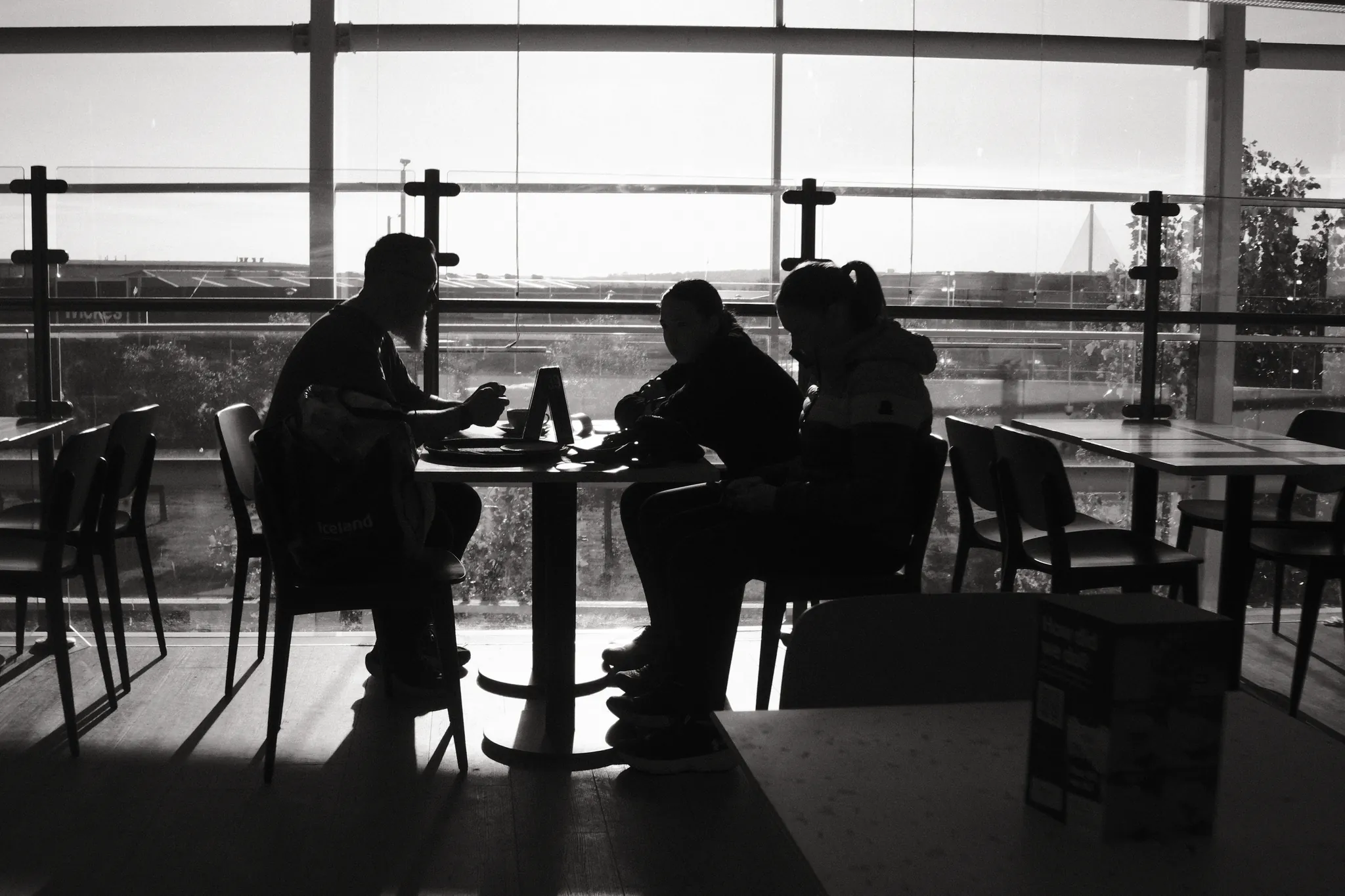 People and cafe tables appear in silhouette against broad windows.