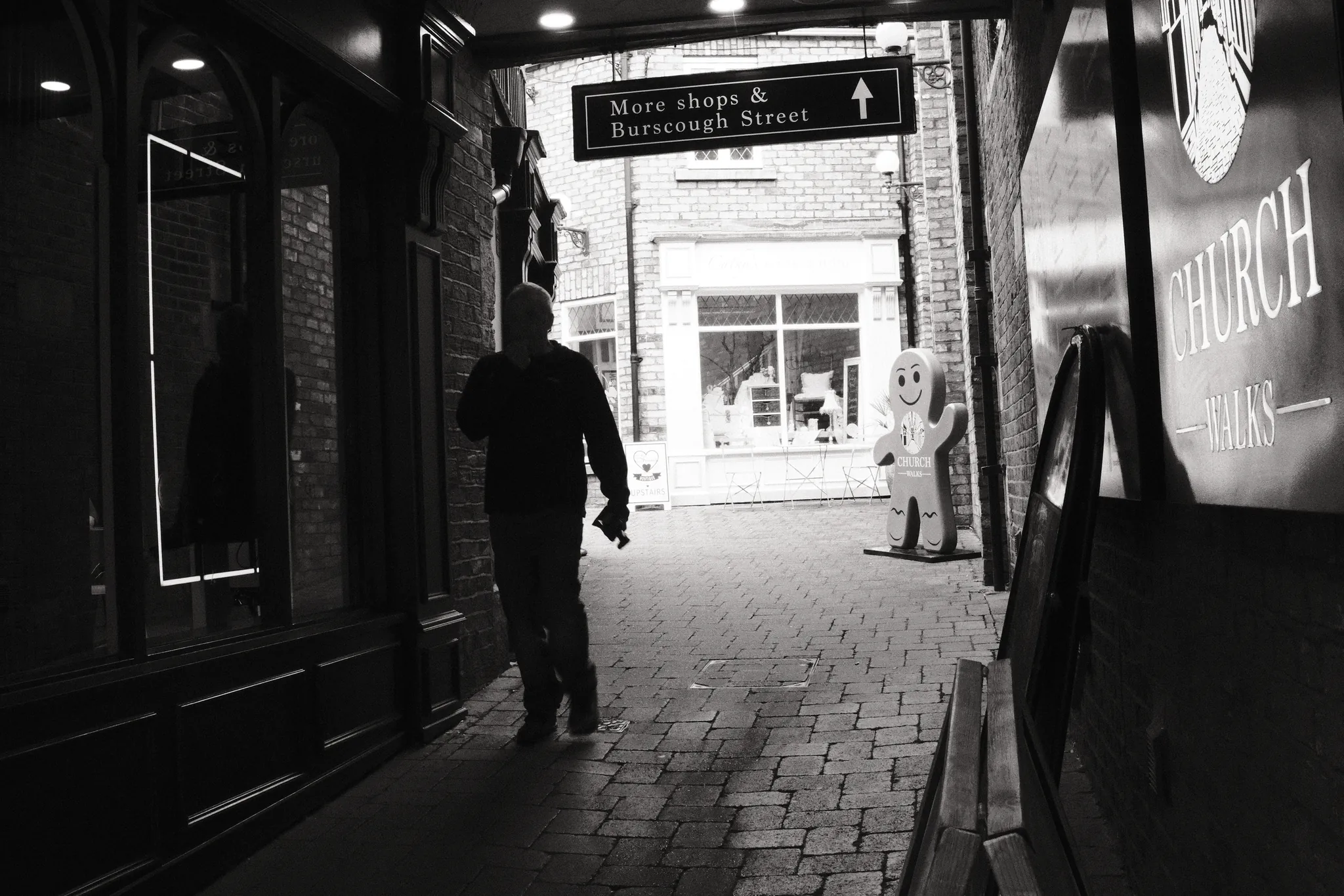 A silhouetted figure crosses Church Walks towards the brighter shops of Burscough Street.