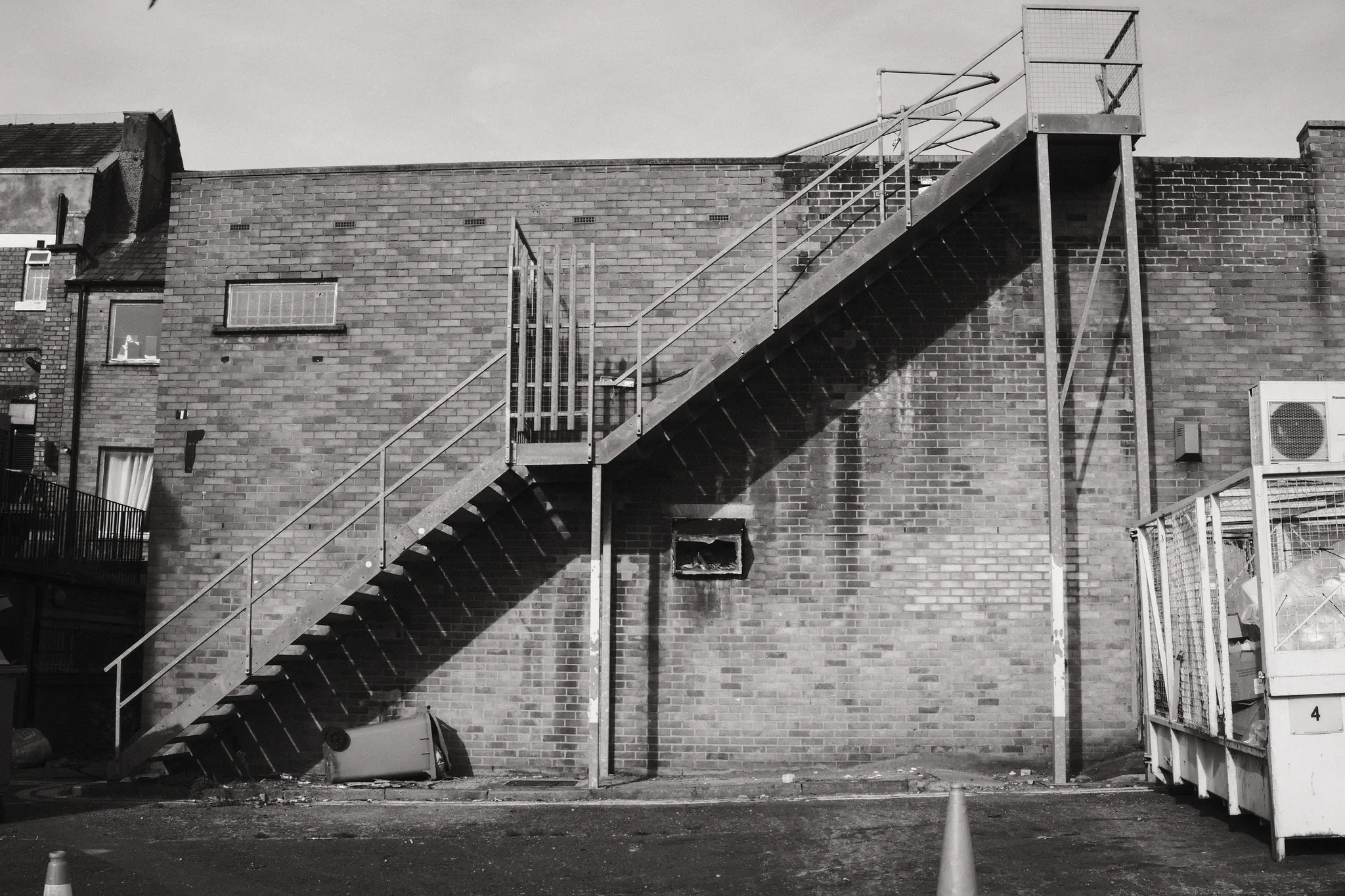 A metal staircase cuts diagonally across a broad brick wall.