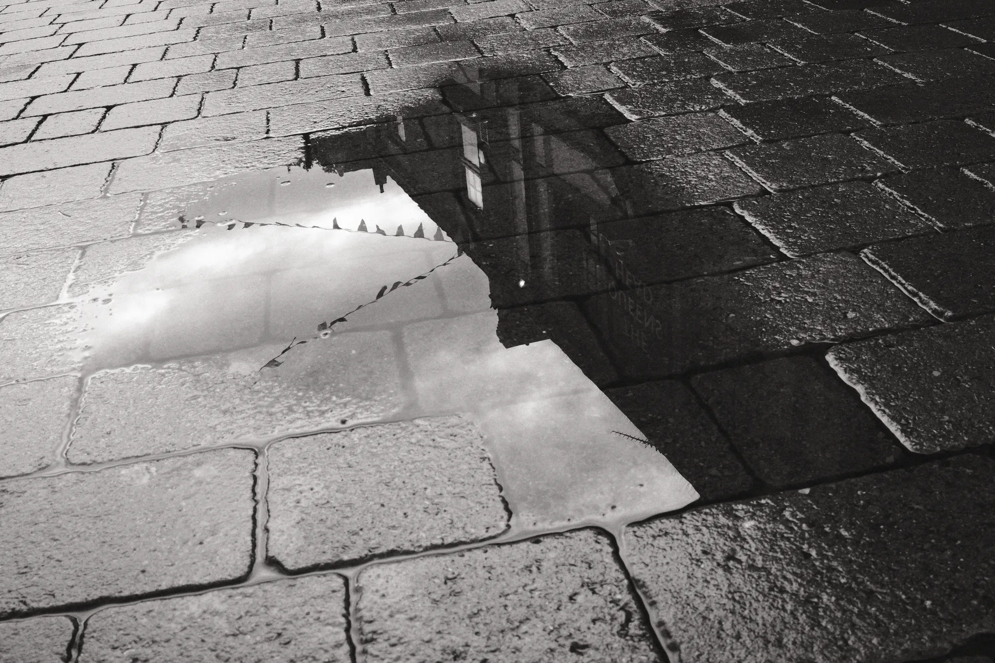 A building is reflected in a shallow puddle between paving stones.