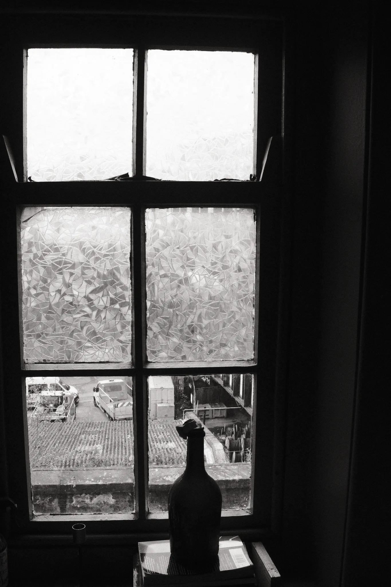 A bottle-shaped silhouette rests on a sill beneath a tall divided window.